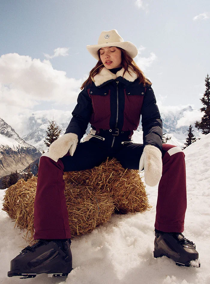 Female model sits on haybale on snowy covered mountains wearing Fusalp skiwear