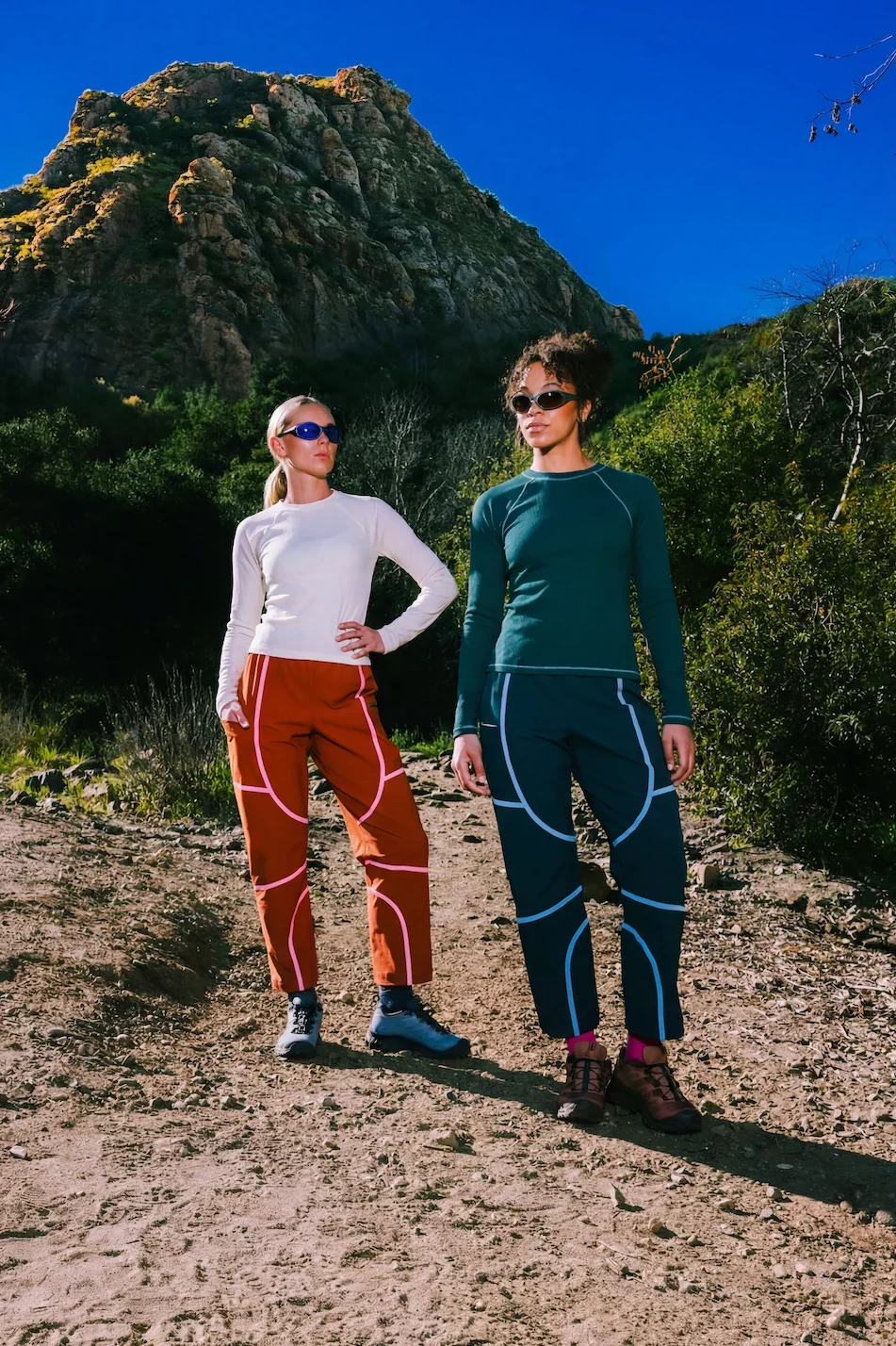 Two women wearing colourful technical hiking trousers with contrasting seam details from women's outdoor clothing brand SENIQ.