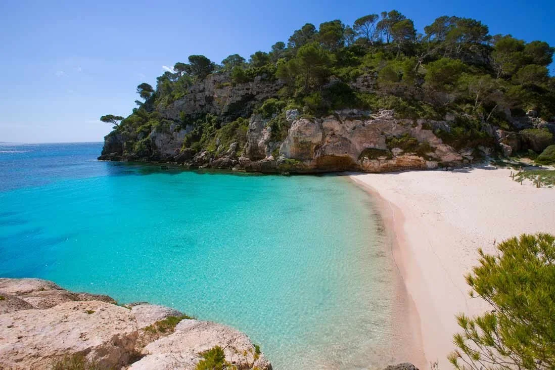 Turquoise water and white sand at a sheltered cove in Menorca.