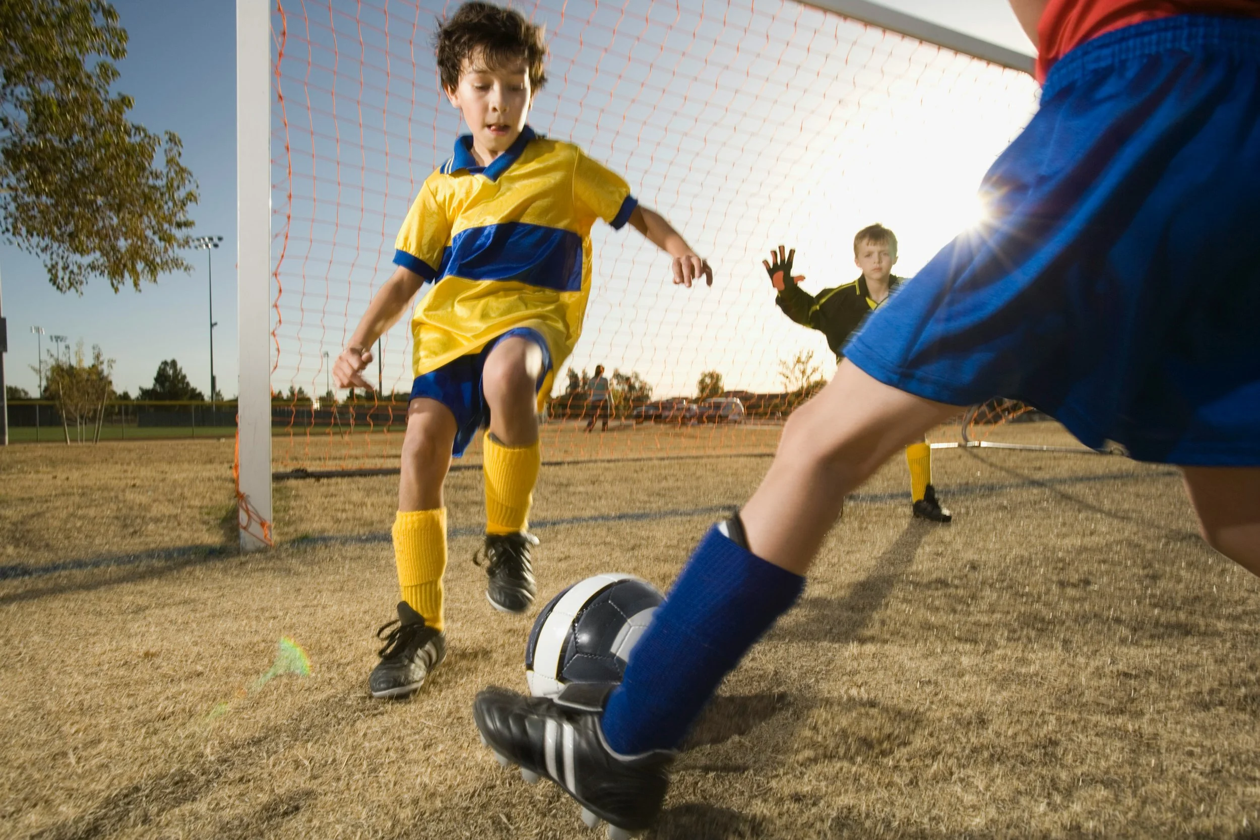 Children competing in a football match, with a young player attempting to win possession near the goal.
