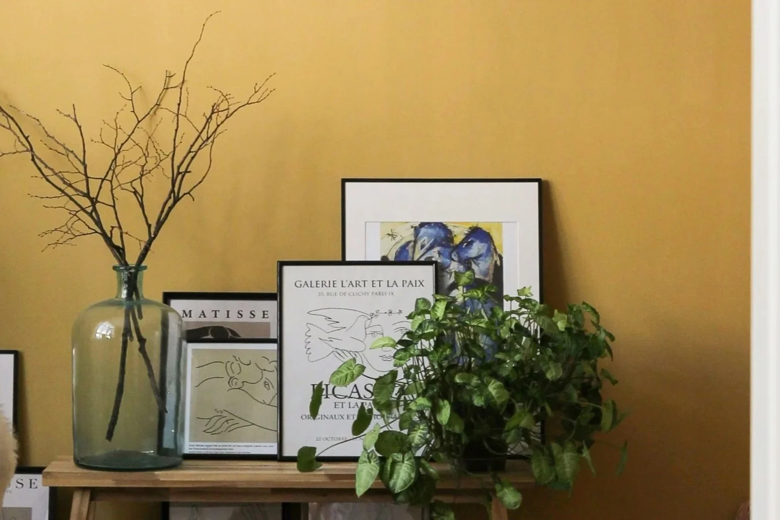 Soft yellow colour-drenched wall with framed artwork, indoor plants and natural wood accents reflecting summer 2026 interior trends
