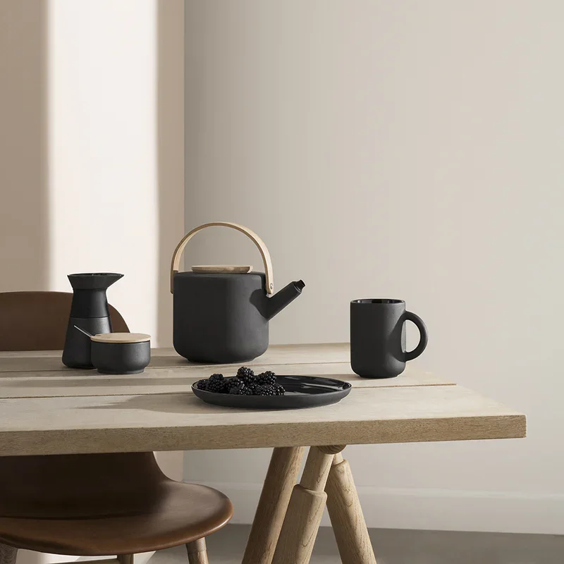 Stelton Theo Tea pot and mug sitting on a wooden table with sunlight beaming through the window.