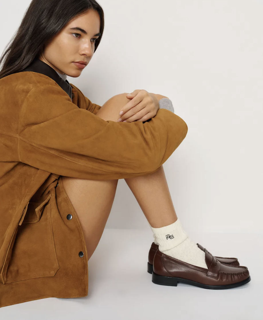 Woman wearing a brown suede jacket with cream socks and brown leather loafers by Reformation.