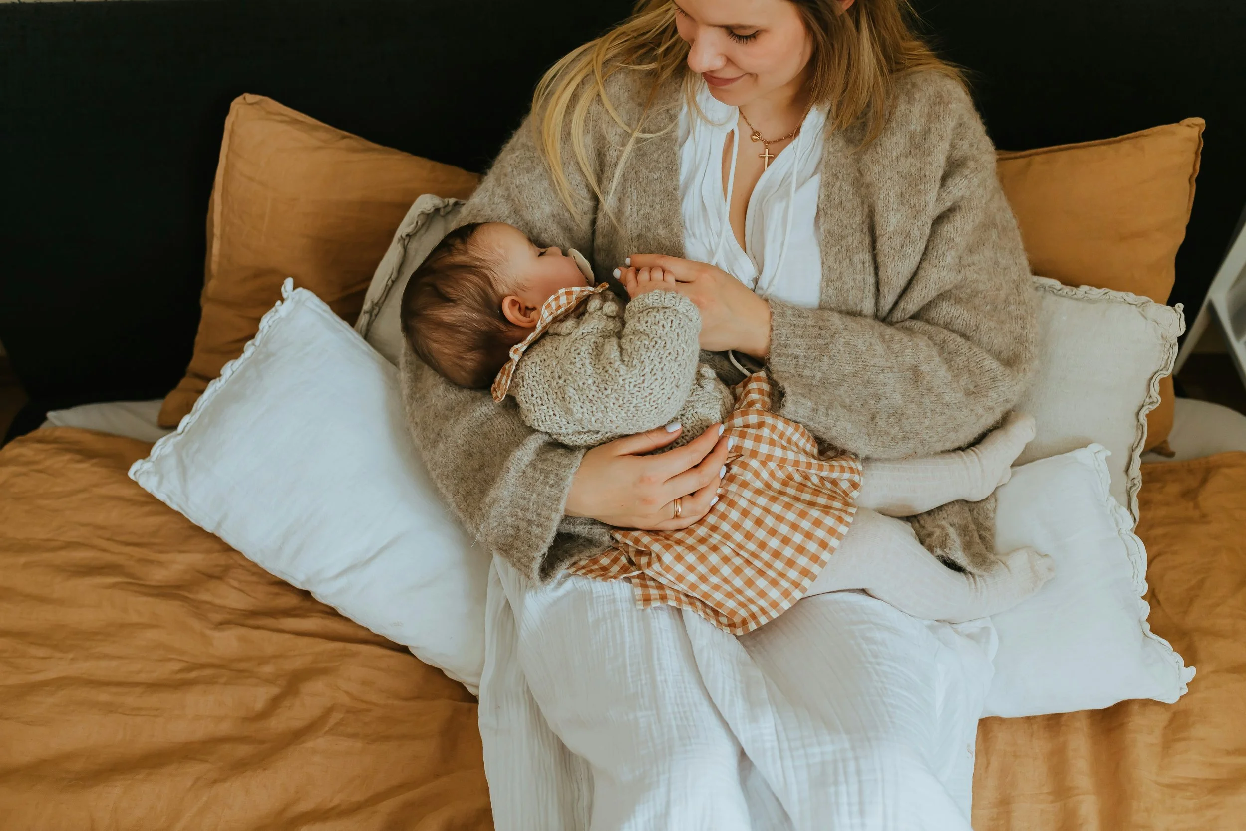 Mother holding her baby on a bed in a calm, neutral-toned bedroom, showing quiet connection and comfort