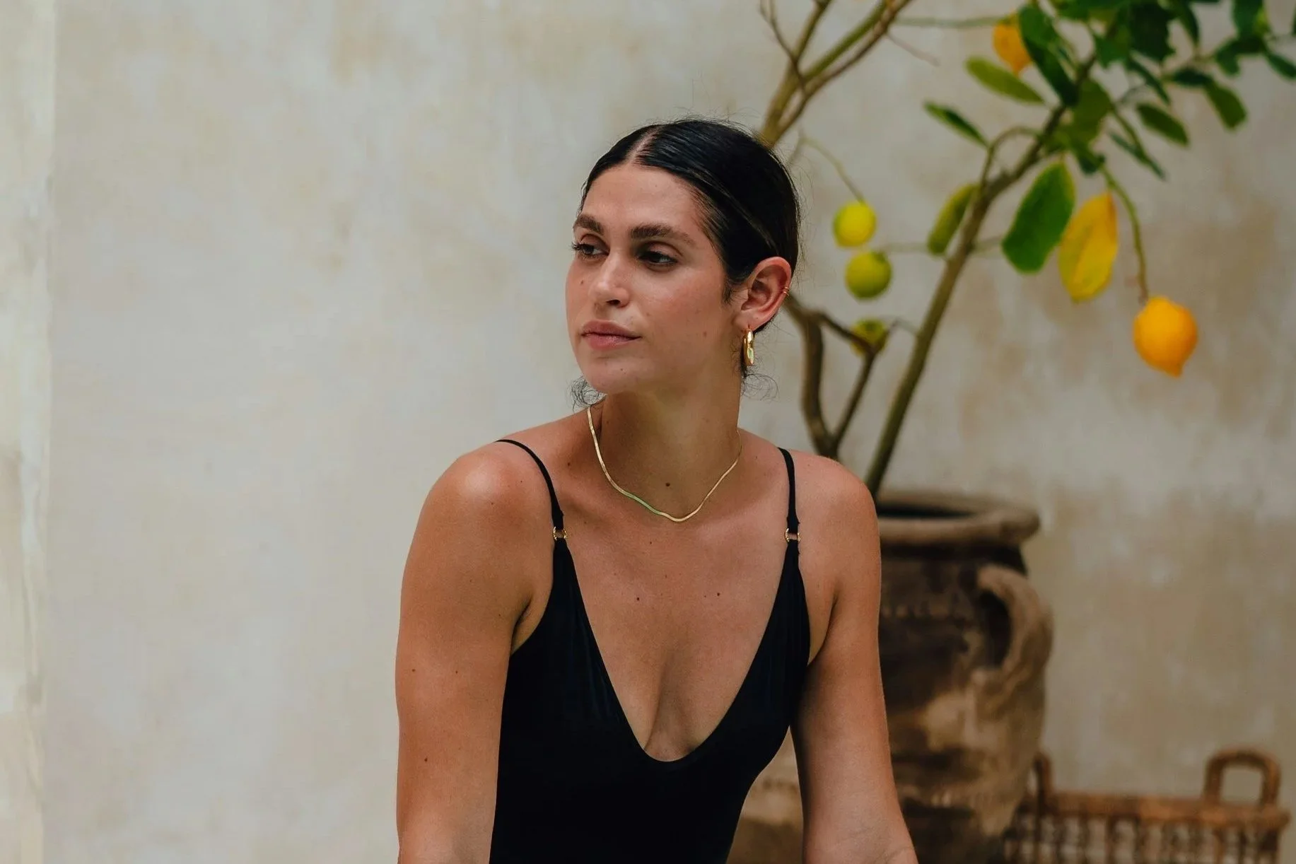 Woman with natural glowing skin sitting outdoors beside a citrus tree, reflecting a fresh, understated post-treatment complexion