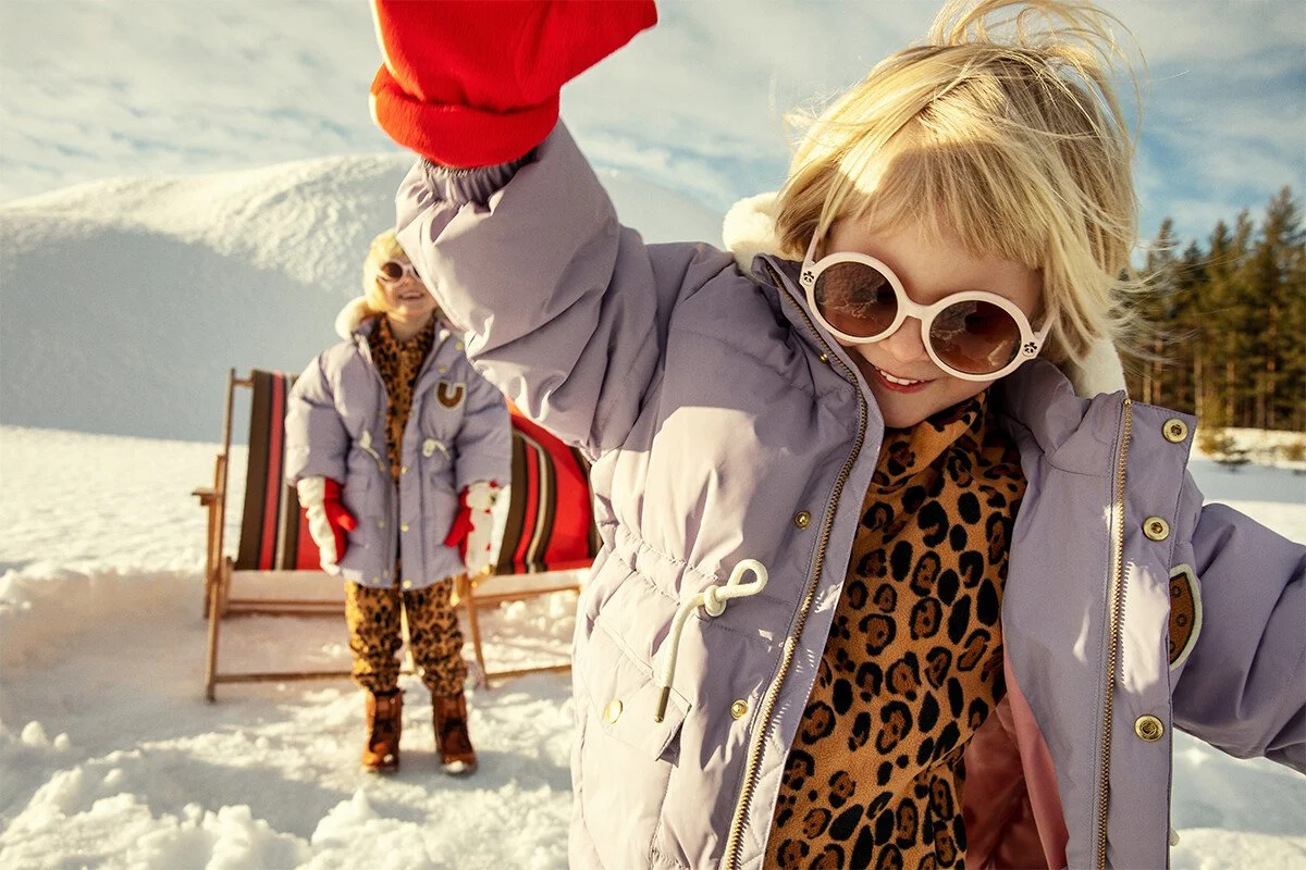 Two twin blonde girls play in the snow wearing Mini Rodini snow wear