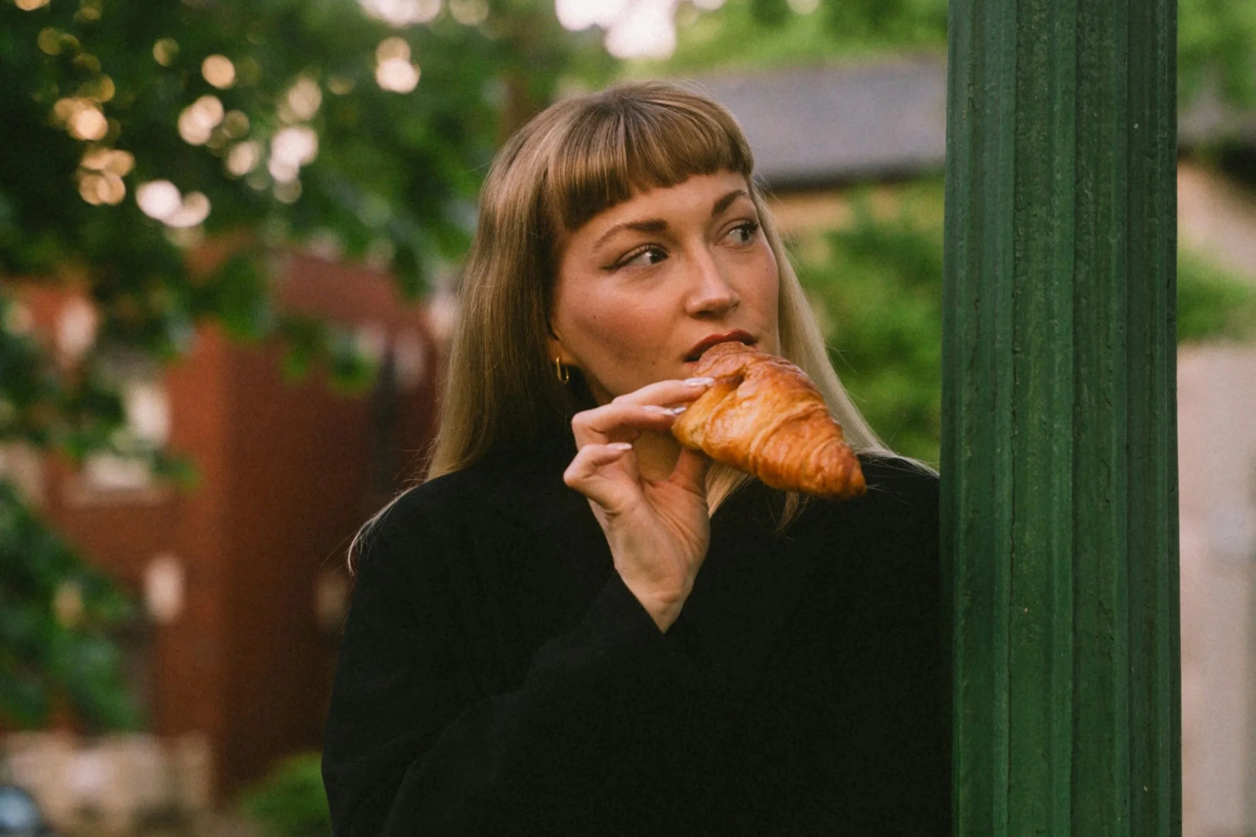 Woman eating a croissant in Paris-inspired surroundings, representing French beauty culture and French pharmacy skincare favourites.