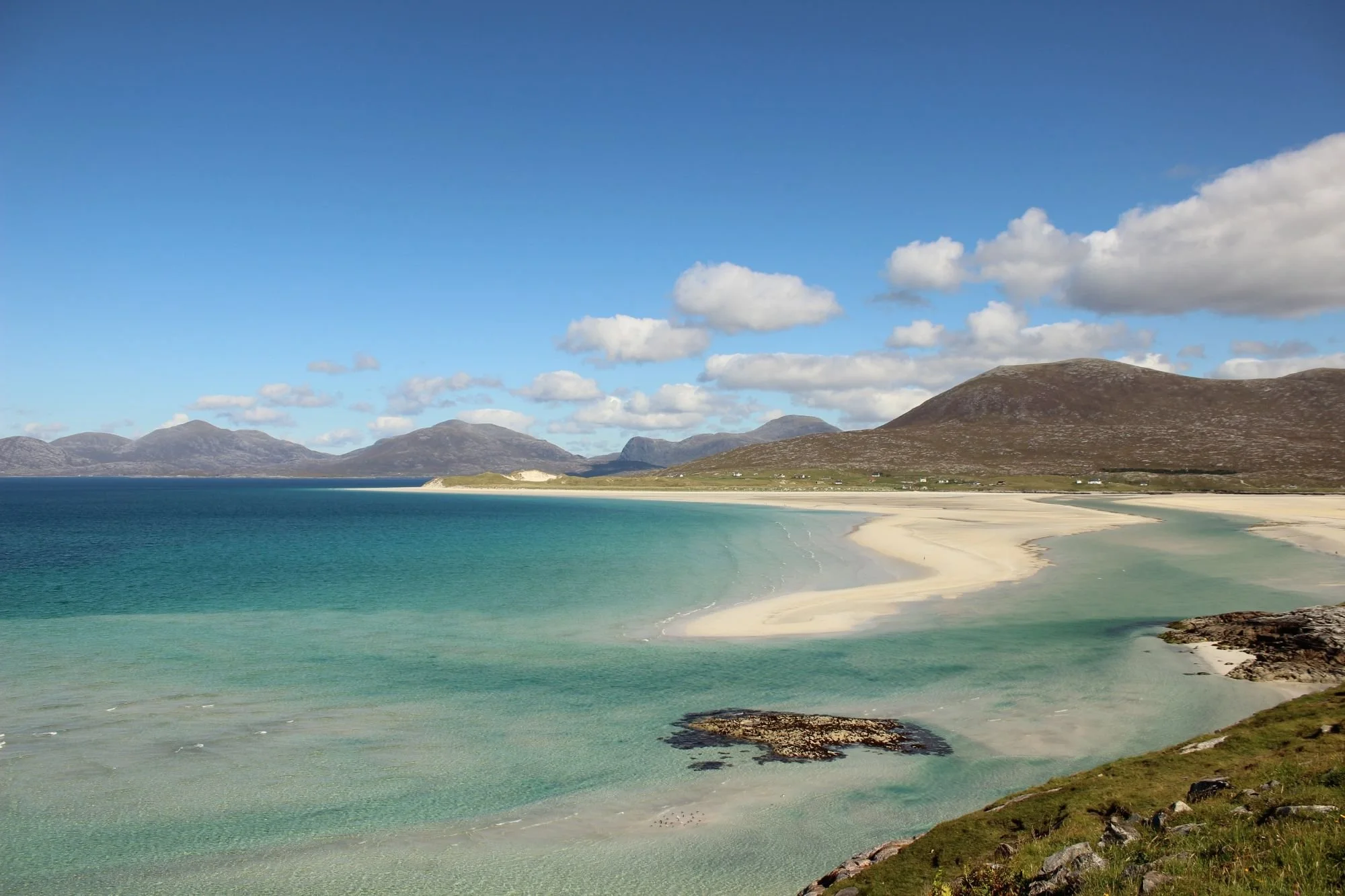 Luskentyre Beach on the Isle of Harris with white sand, clear turquoise water and mountain backdrop.
