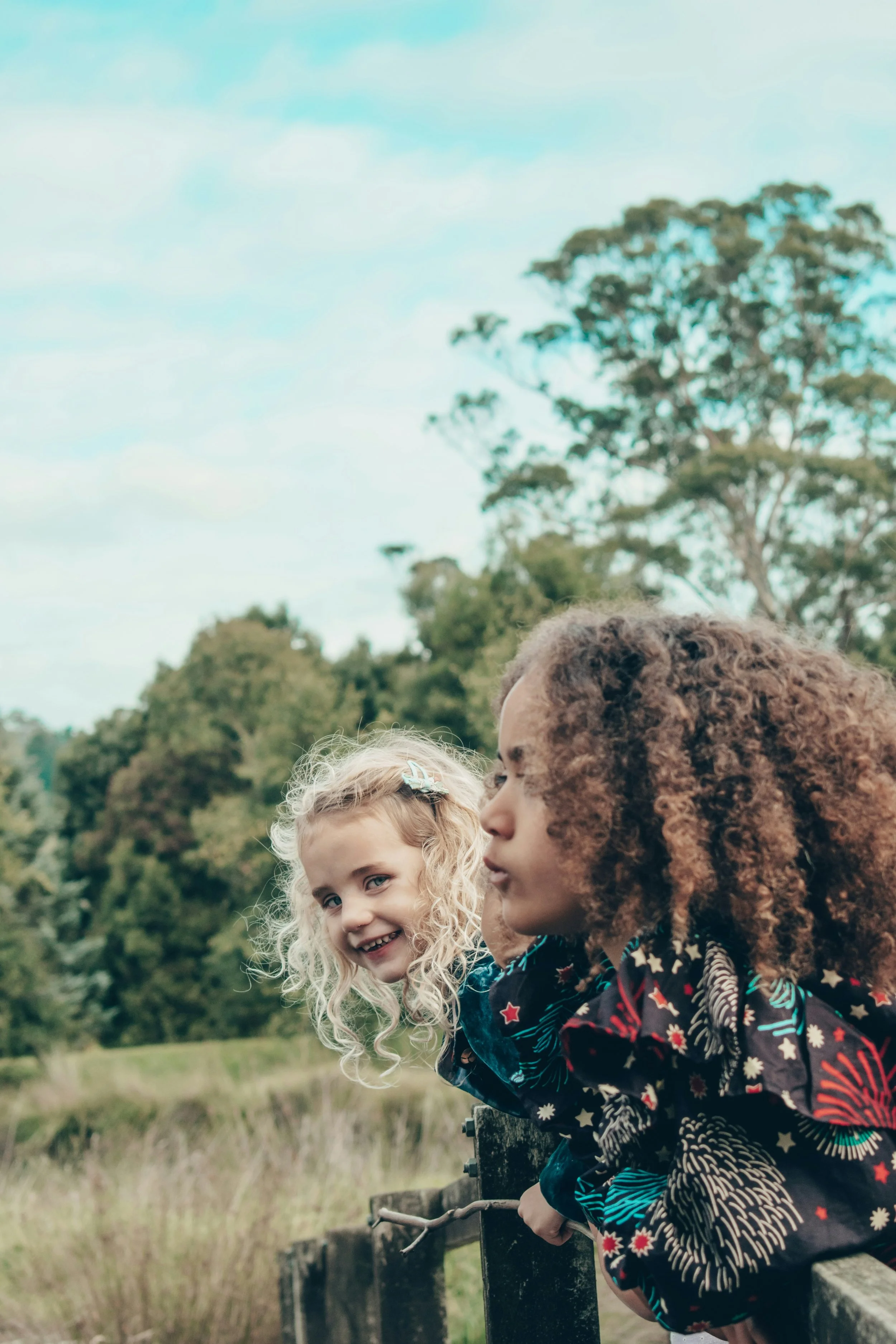 Two young girls talking together outdoors by a wooden fence