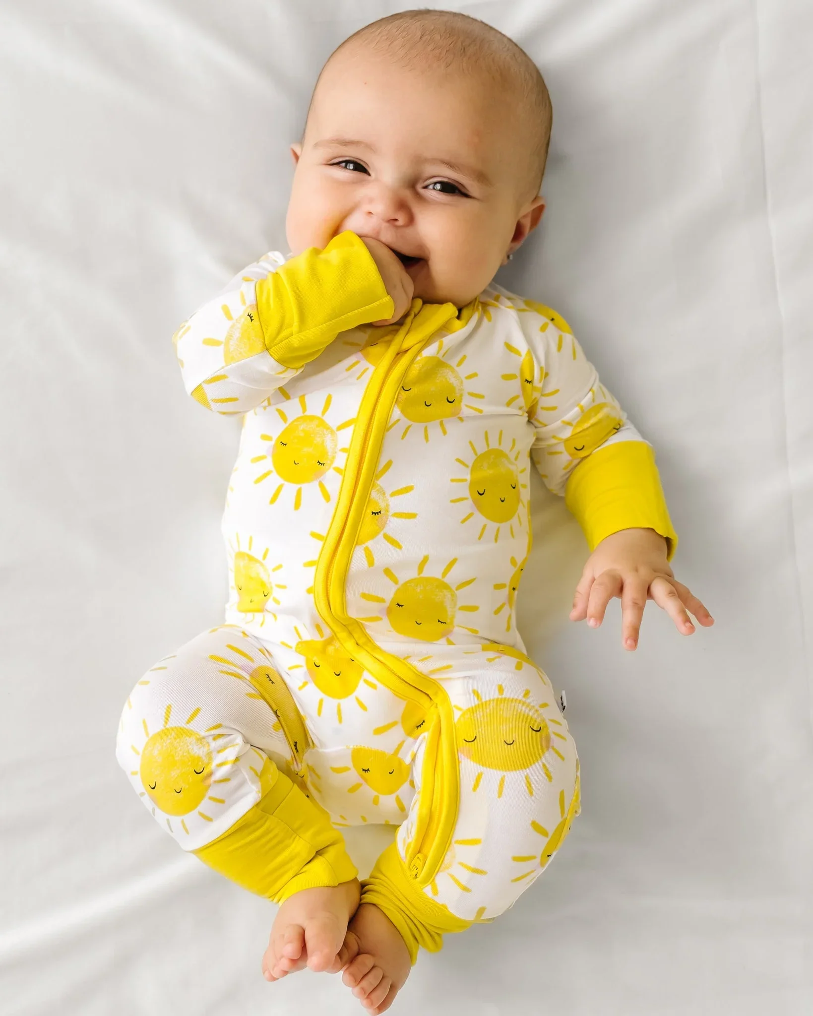 Smiling baby wearing yellow sun-print bamboo pyjamas. by little sleepies