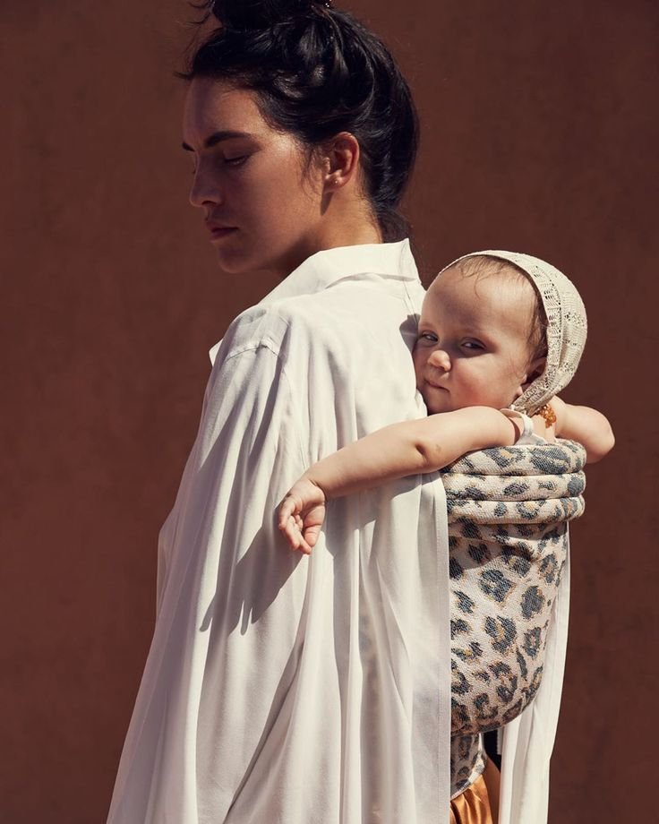 Mother wearing Artipoppe leopard print baby carrier during summer travel
