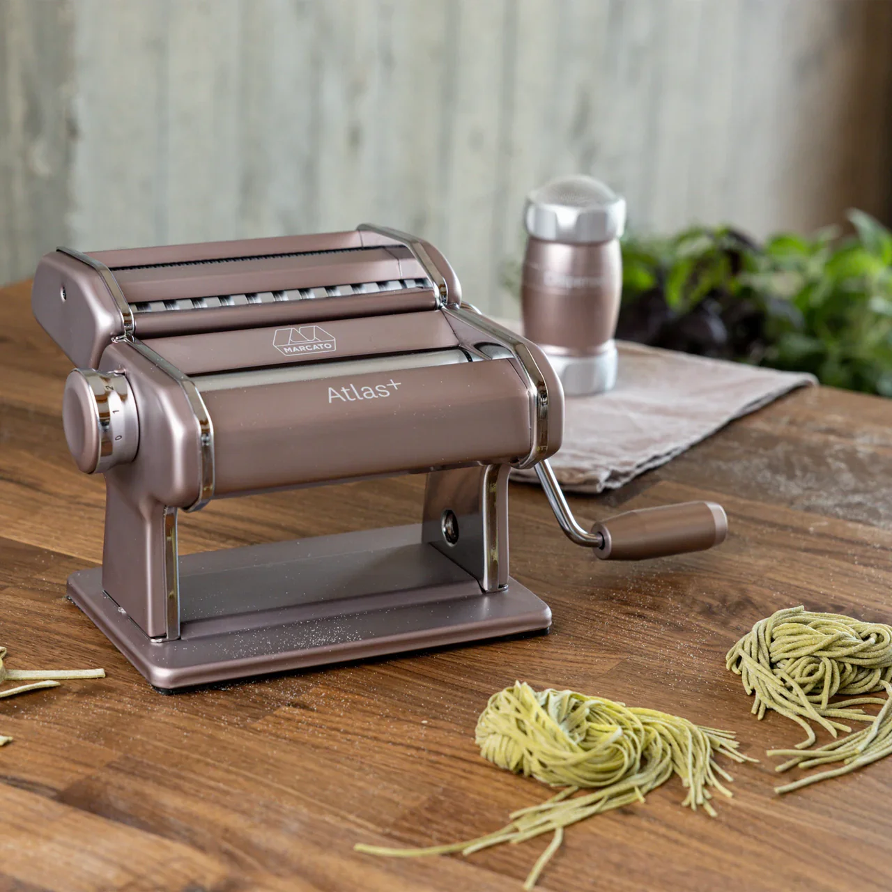 Pink Mercato Atlas Pasta Maker on a wooden table with piles of freshly made  spaghetti