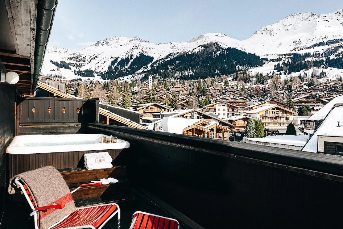 Chalet balcony with hot tub and view of snow covered mountains and village at the  Experimental Chalet Verbier, Switzerland