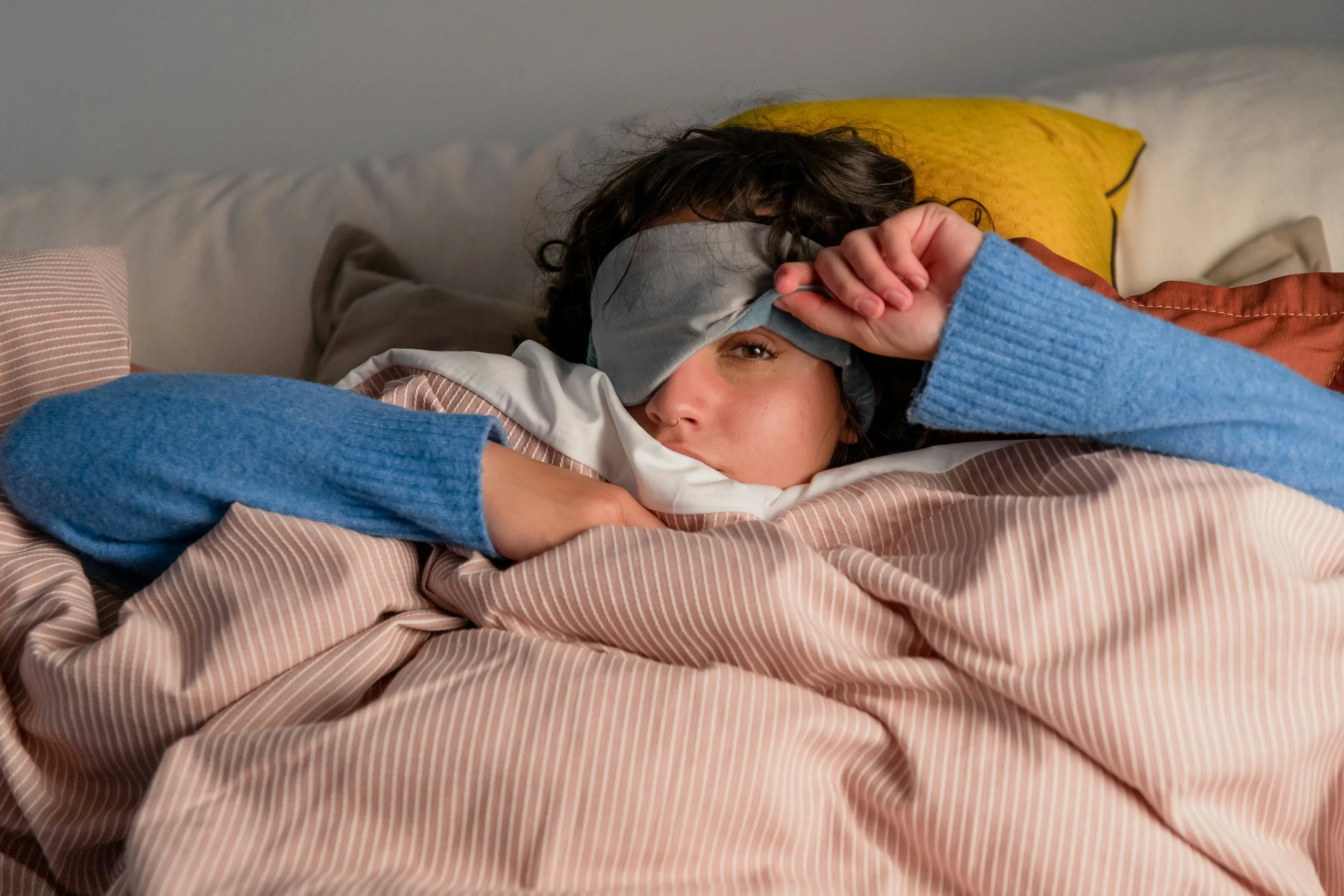 Woman lying in bed wearing a sleep mask, representing disrupted sleep and hormonal insomnia during perimenopause.