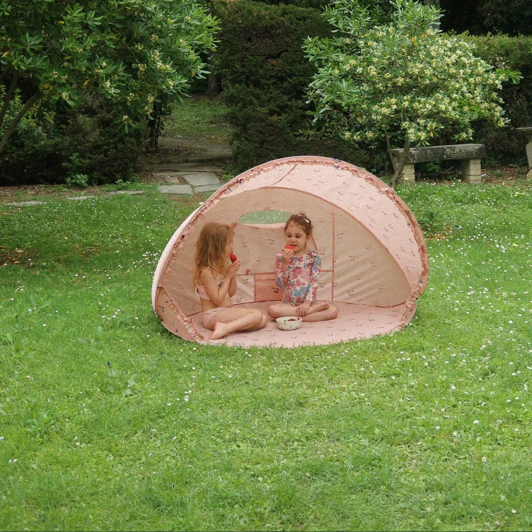 Two girls sit in the garden eating watermelon inside Konges Sløjd's Pop-Up UV Tent