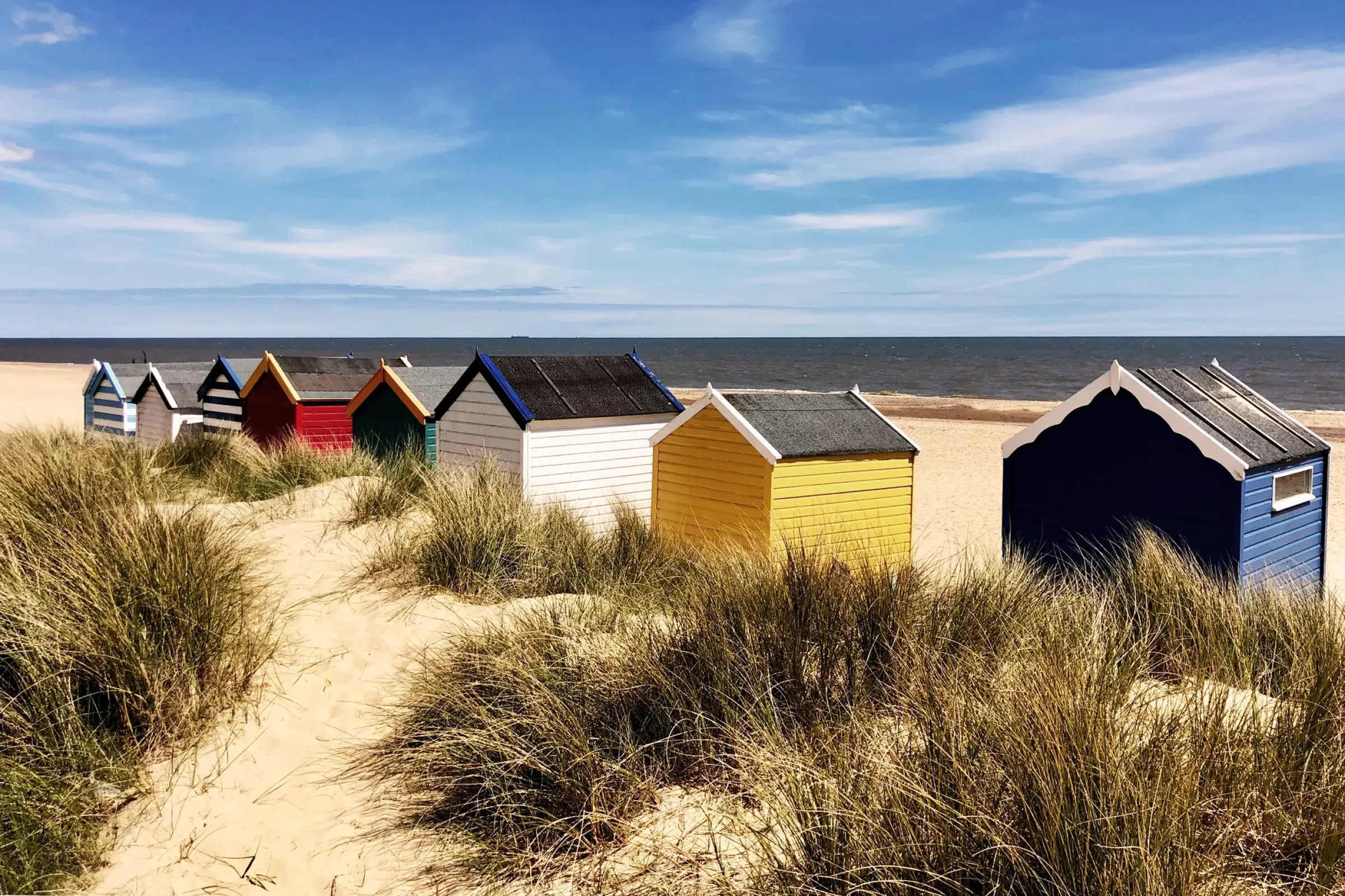 Colourful beach huts set amongst dunes at Walberswick Beach on the Suffolk coast.