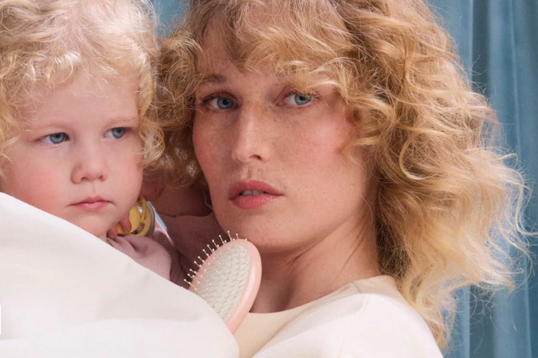 Woman with textured blonde hair holding a child and La Bonne Brosse hairbrush, illustrating postpartum and hormonal hair changes in women in their thirties and forties.