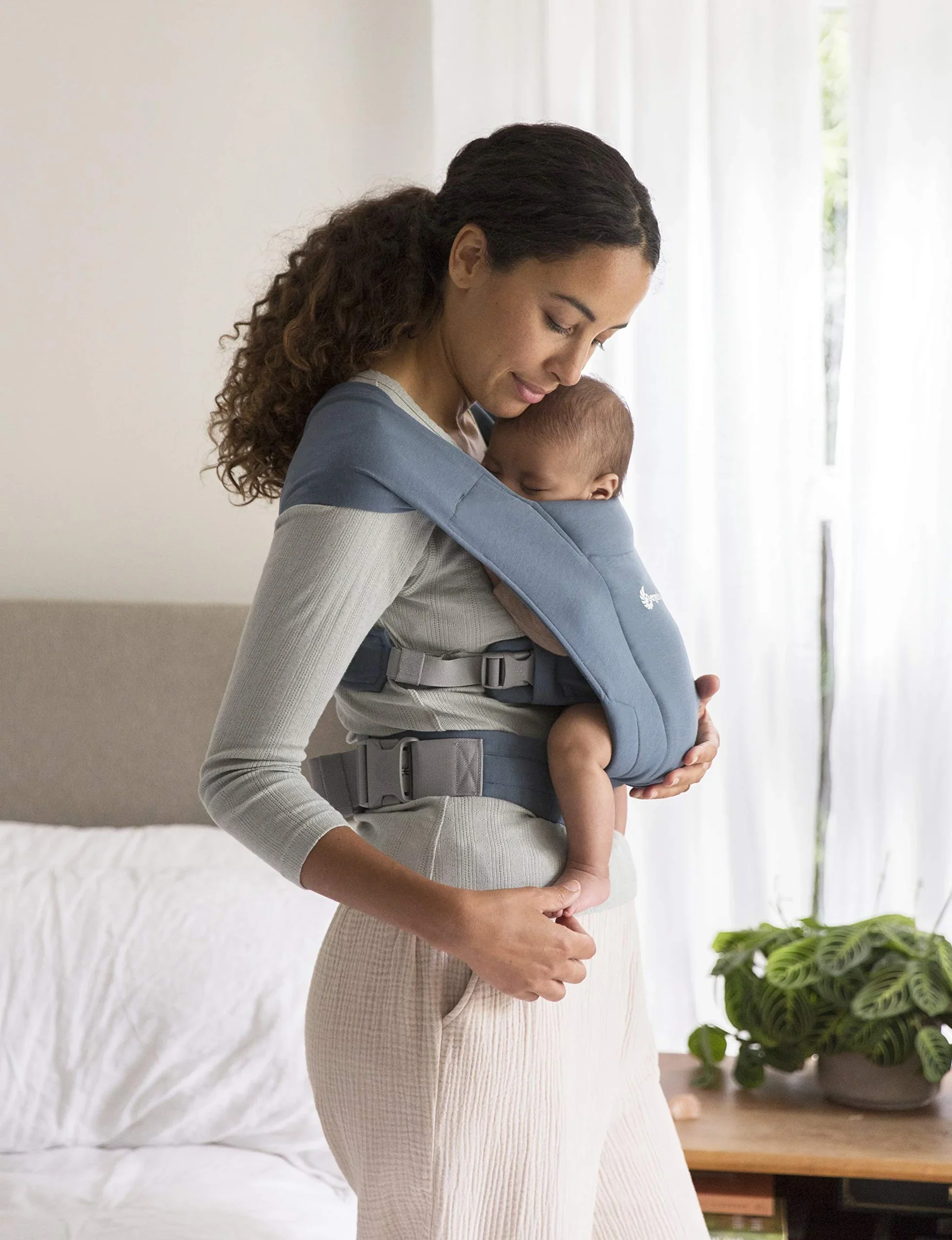Mother carrying a sleeping newborn in a blue Ergobaby Embrace soft baby carrier