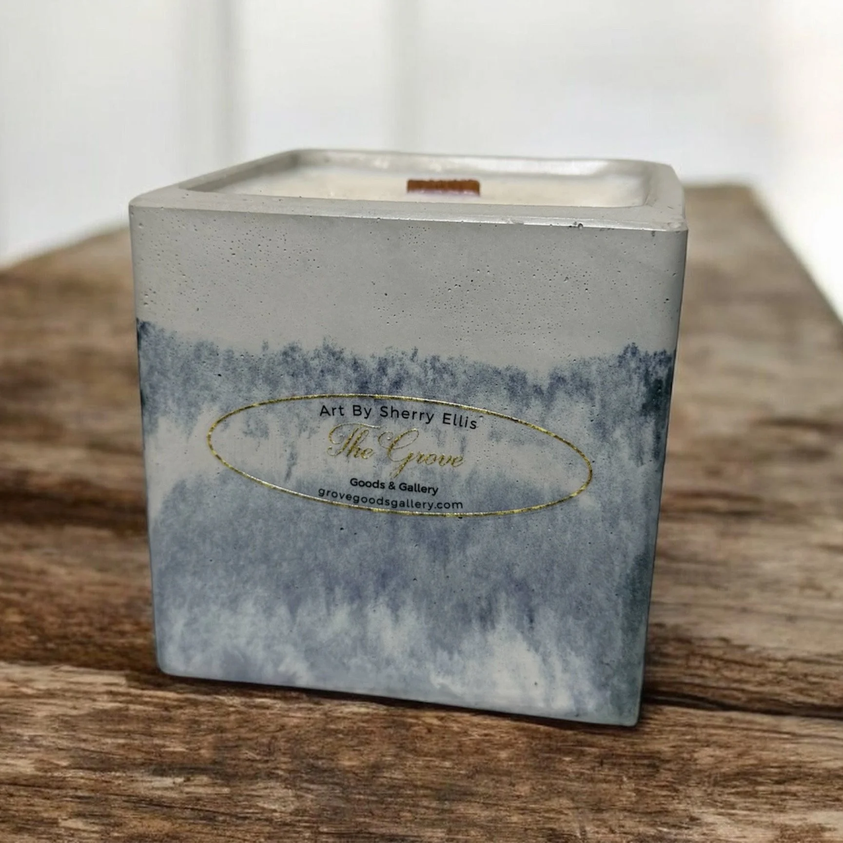 Large square soy wax candle with a wooden wick in a marbled blue cement vessel.