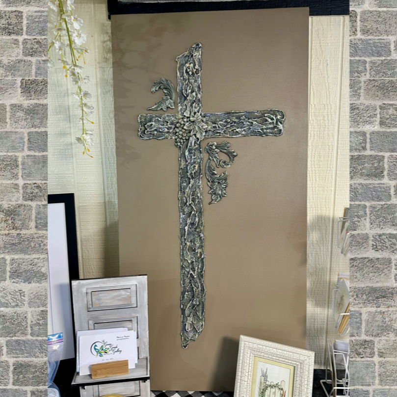 Decorative cross made of snakes on a beige background, displayed in an indoor setting with framed pictures and decorative items around.