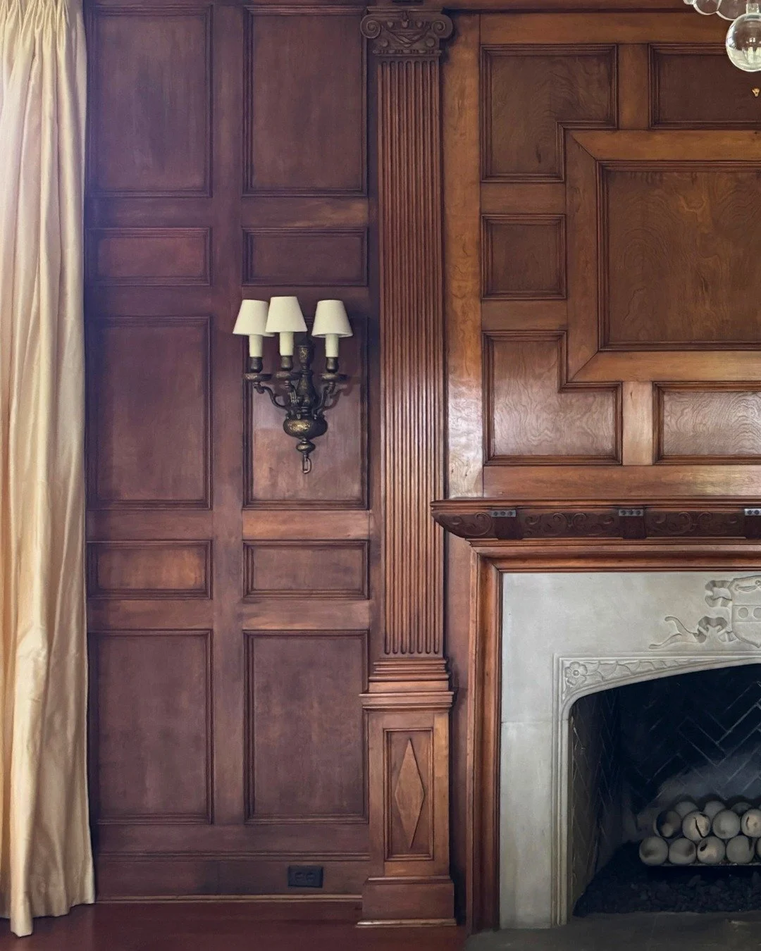 Within Riverview Renewal: A Legacy Project, this living room centers around an original fireplace in a 1920s home designed by Pringle and Smith in the Medieval Revival tradition. 

Floor-to-ceiling wood paneling, a Jacobean strapwork plaster ceiling,