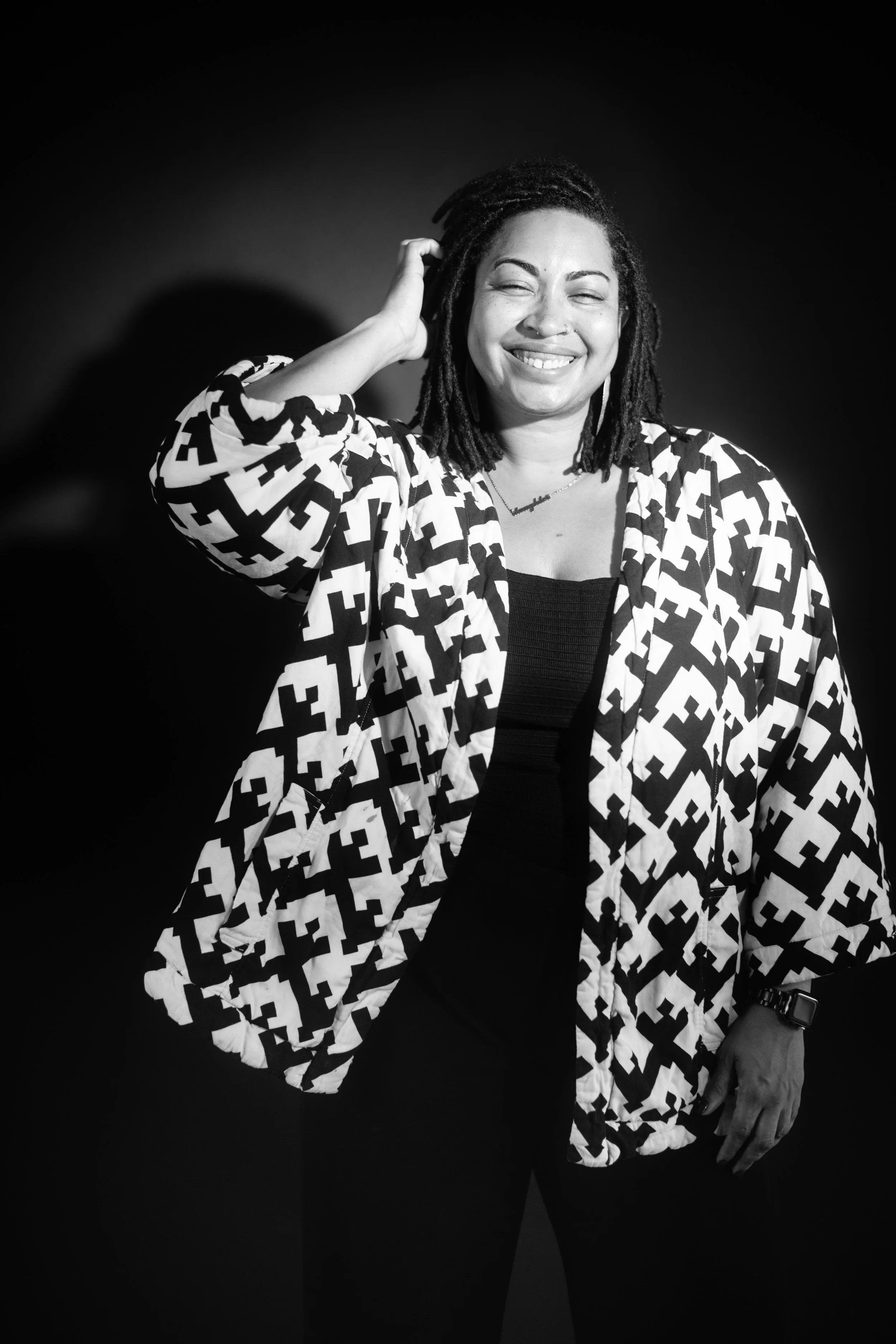 A woman is smiling wearing a houndstooth jacket in front of a black background.