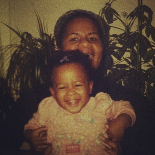 Mother with a baby on her lap sitting in front houseplants. They are both laughing and looking at the camera.