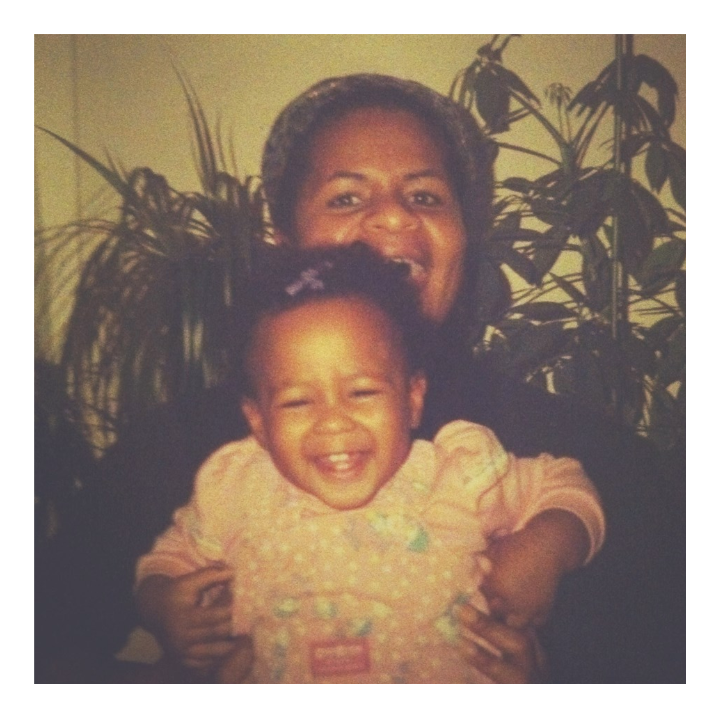 Mother with a baby on her lap sitting in front houseplants. They are both laughing and looking at the camera.