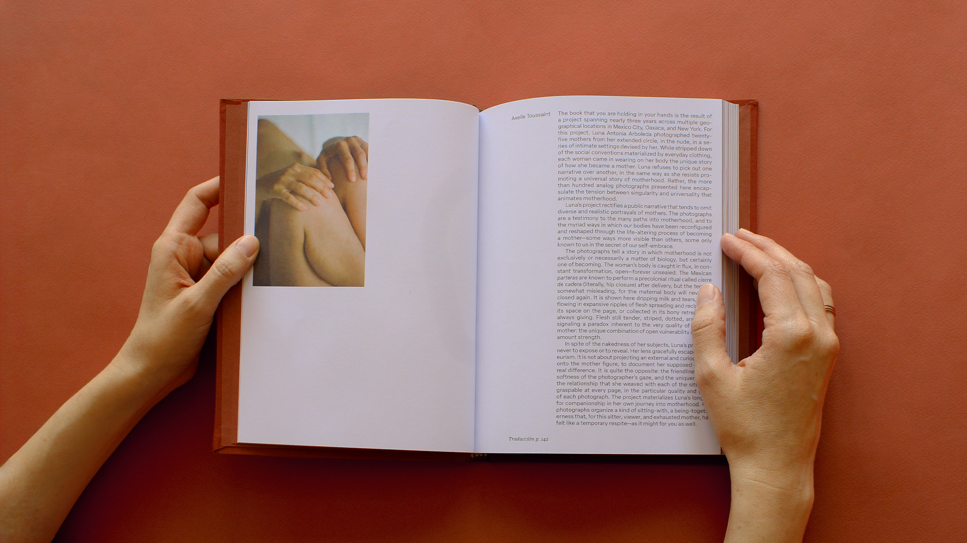Hands hold open a copy of Madre against a terracotta backdrop, revealing an intimate portrait alongside the book’s introductory essay about motherhood and transformation.