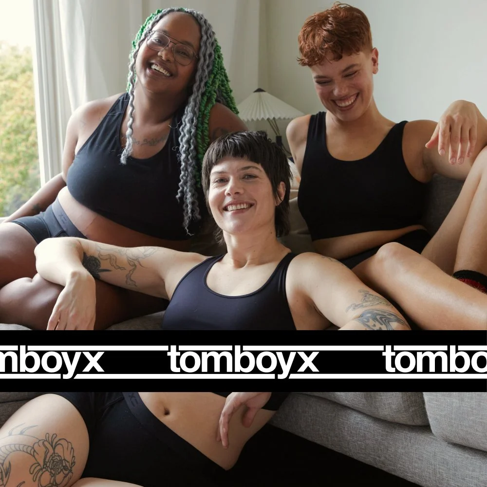 Three people wearing black underwear sitting on a couch and smiling.