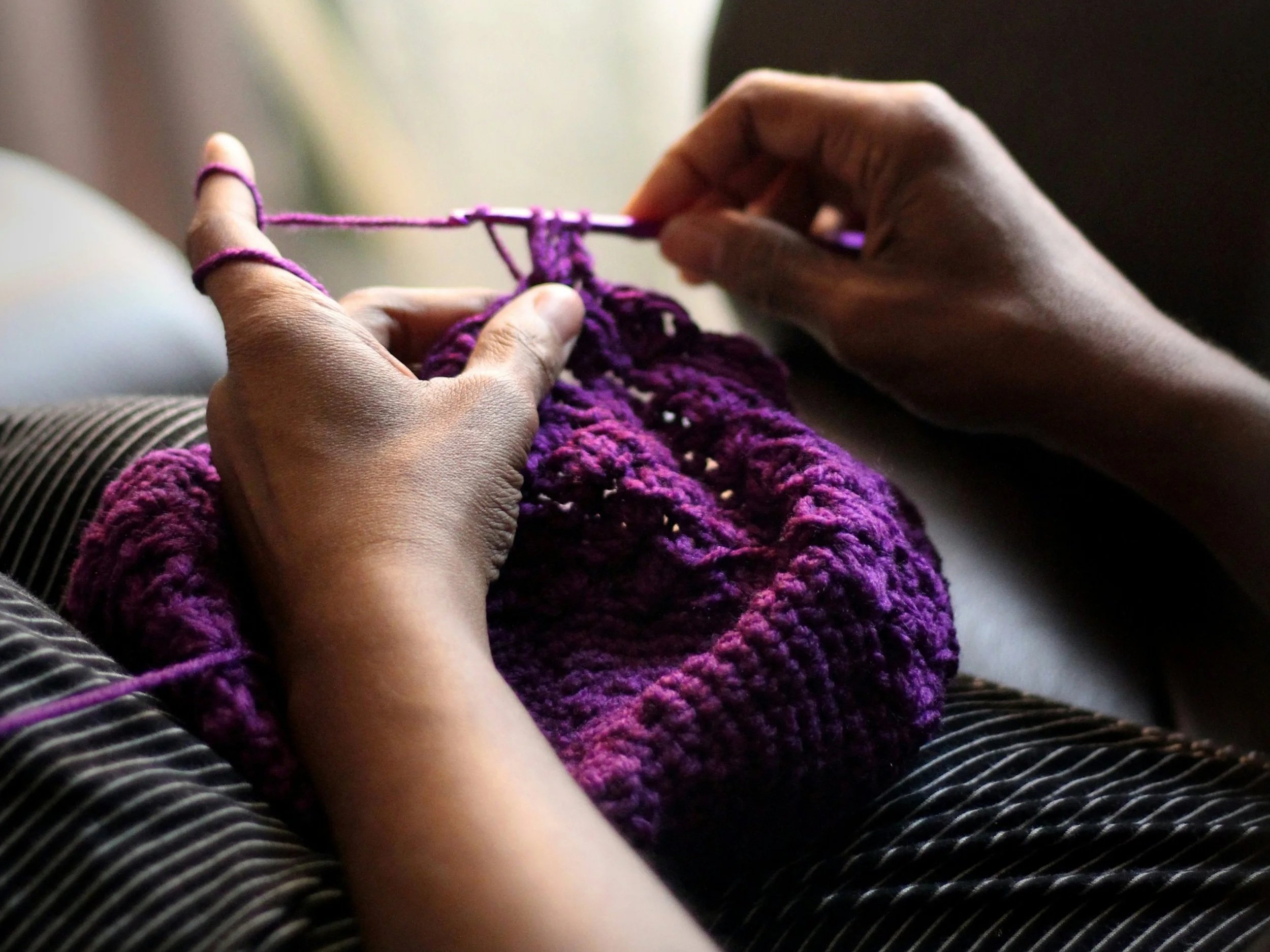 Hands crocheting a purple hat.