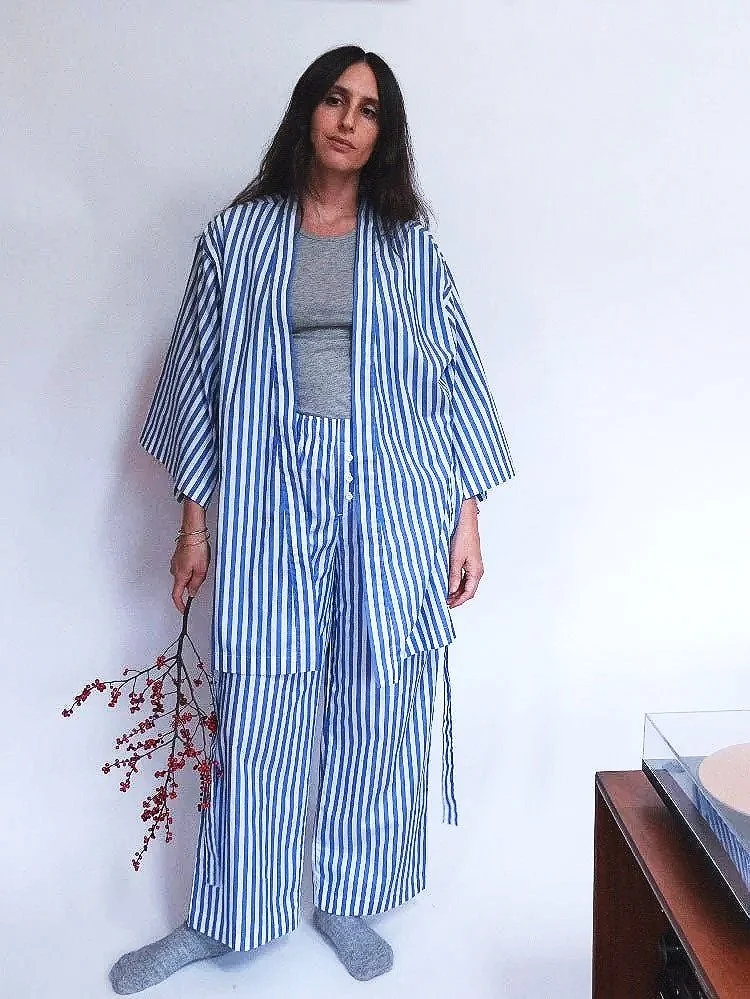 A woman wearing a blue and white striped robe, holding a stick with red flowers in one hand.