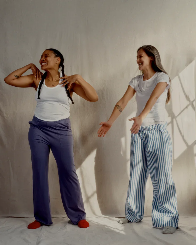 Two woman are standing in front of a white wall wearing pajamas.