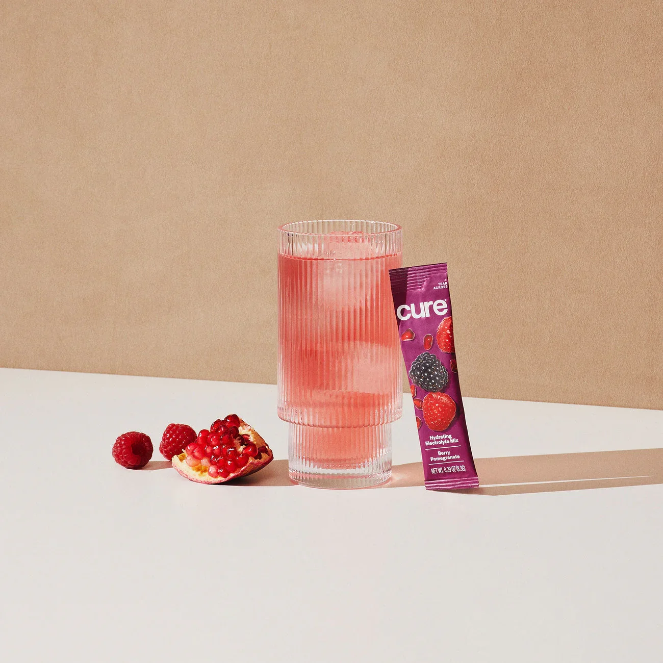 A glass on a table with an electrolyte package leaning on it and fruit beside it.