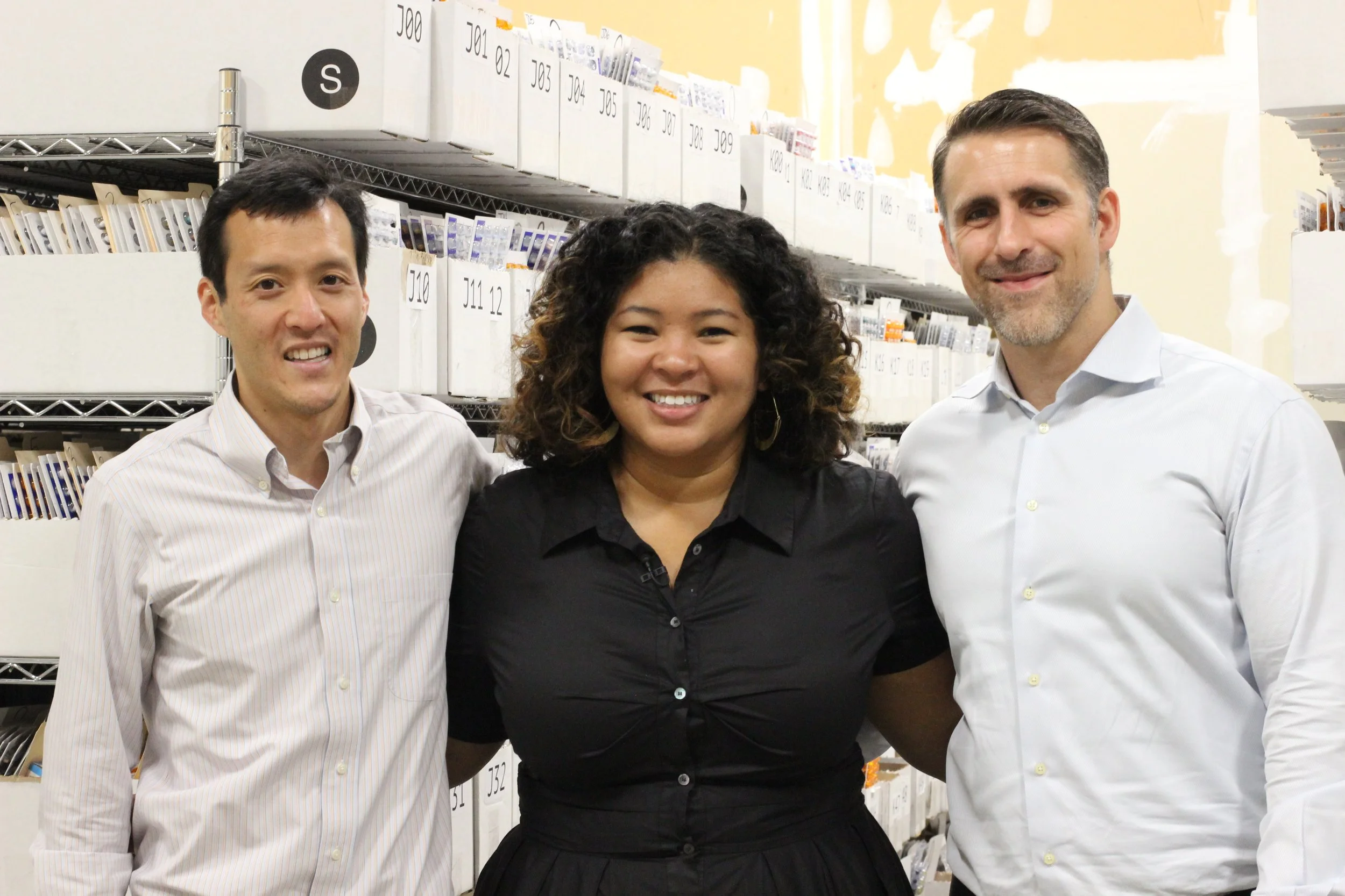 Three colleagues smile together in an organized archive storage area, showcasing a collaborative and professional team environment.