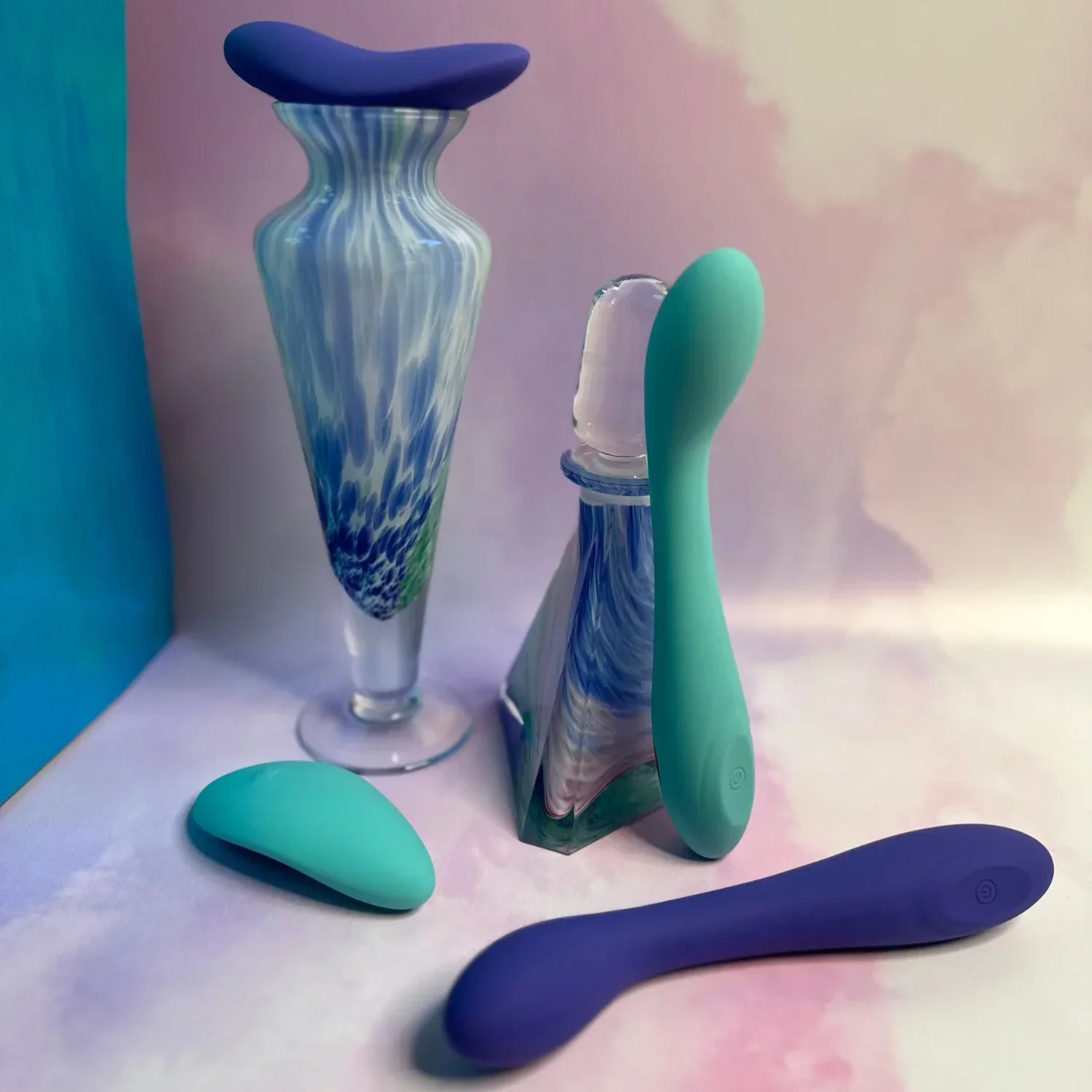 A curated arrangement of body-safe sex toys in soft blue and green tones is styled alongside decorative glass objects, highlighting Spectrum’s modern and inclusive approach to pleasure.