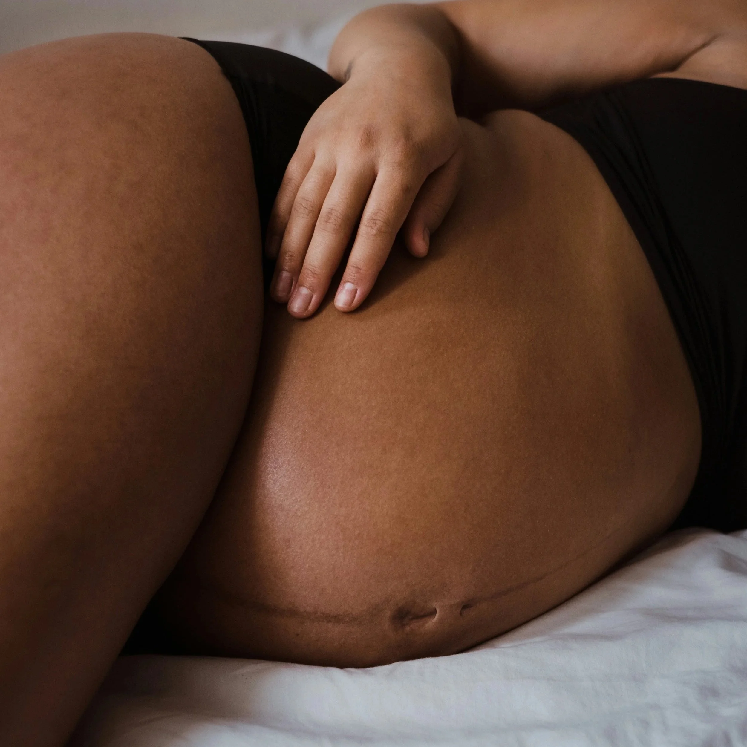 A pregnant woman laying on her side wearing black underwear.