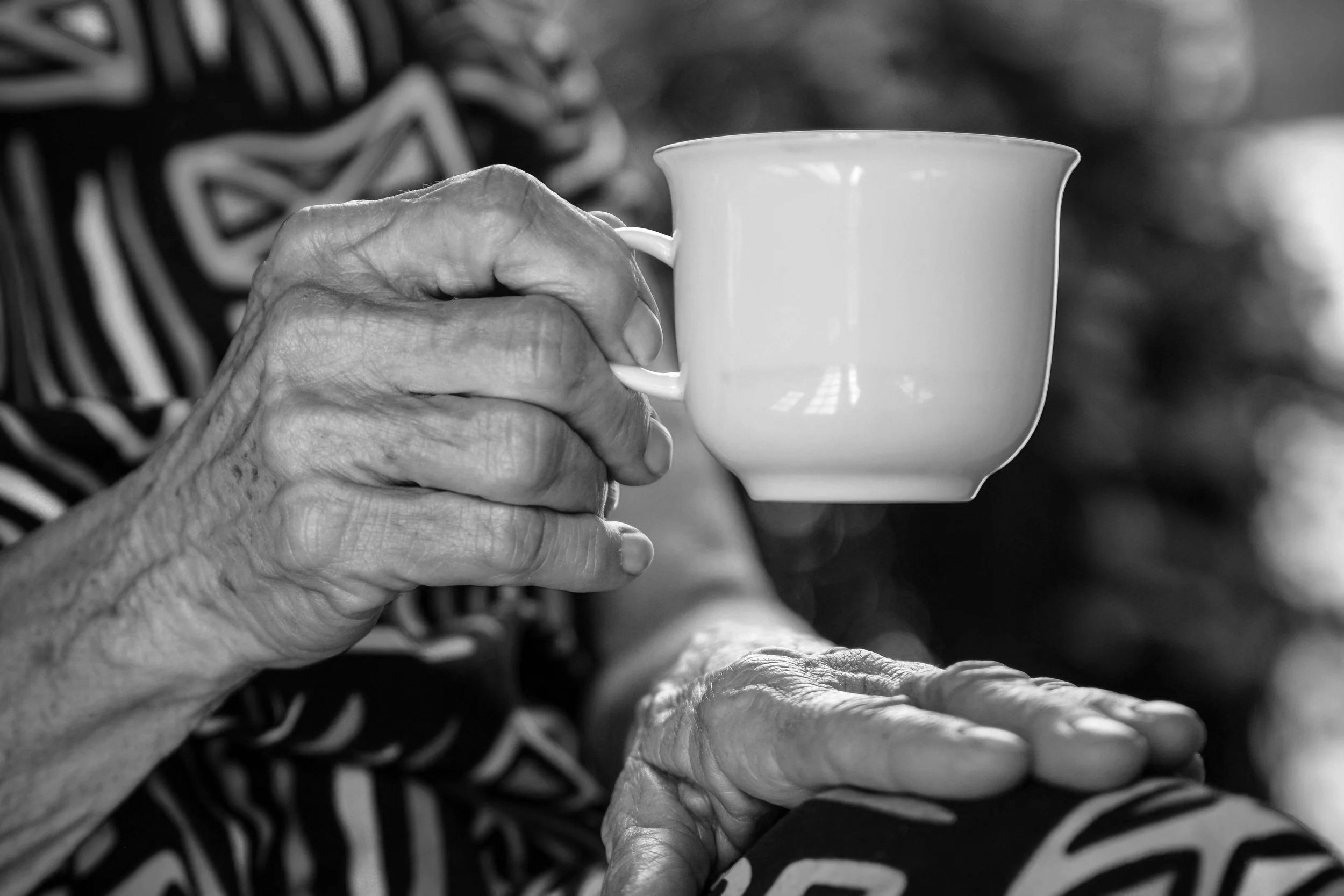 An old person wearing a patterned dress is holding a cup of tea