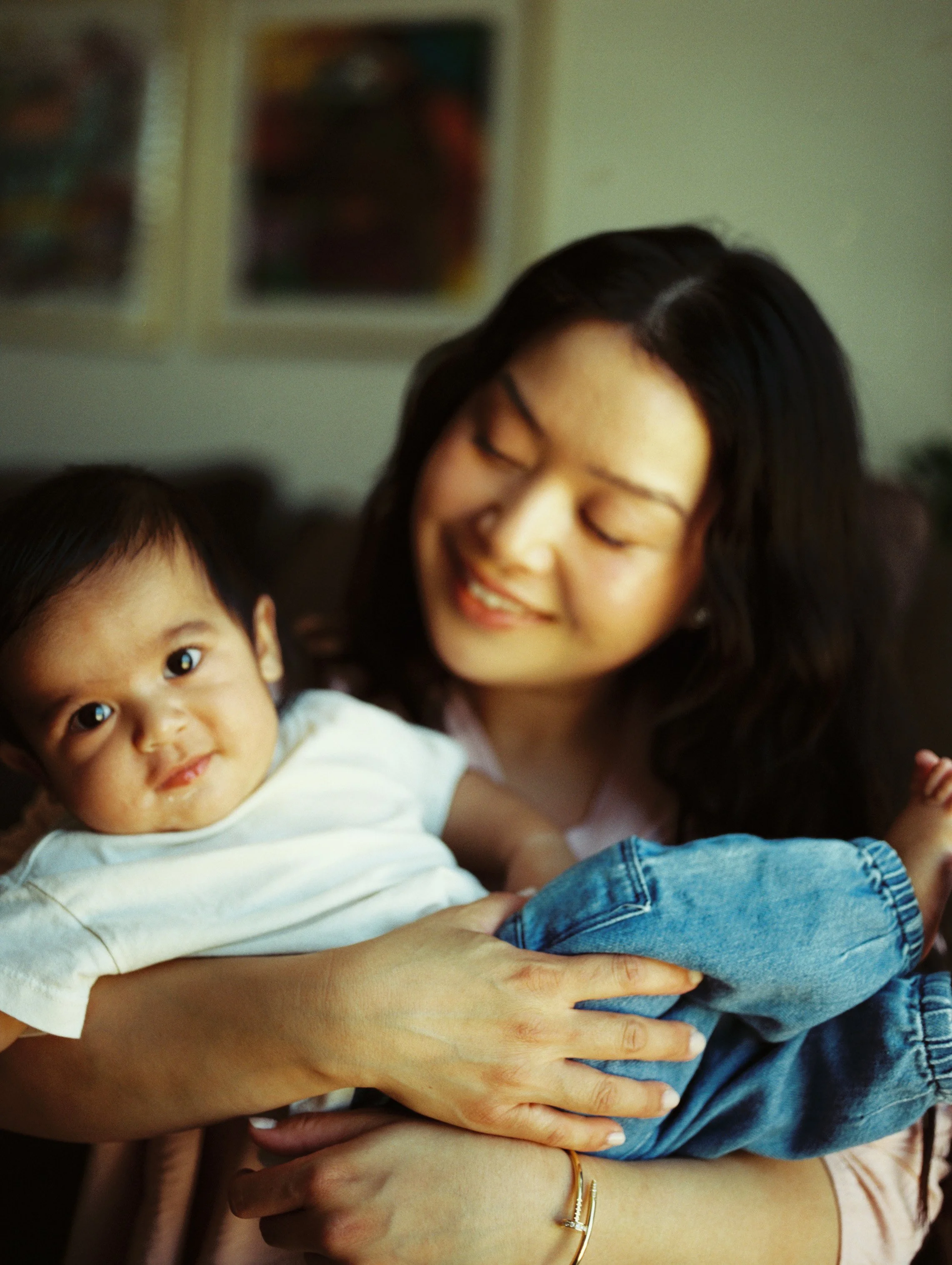 An Asian woman is holding her son while he smiles and looks at the camera.