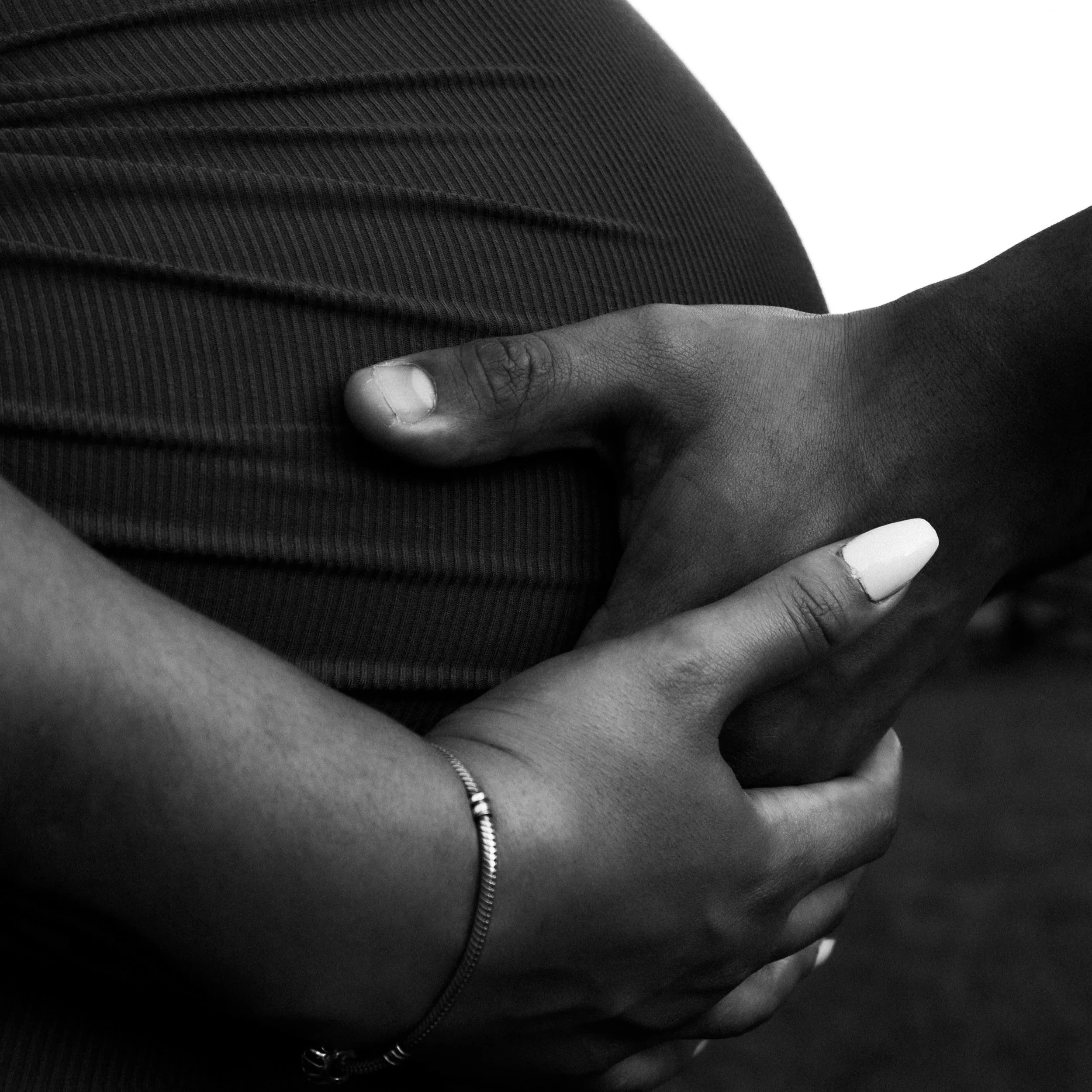 A black and white photo of a hand cupping a pregnant belly with another hand on top of it.