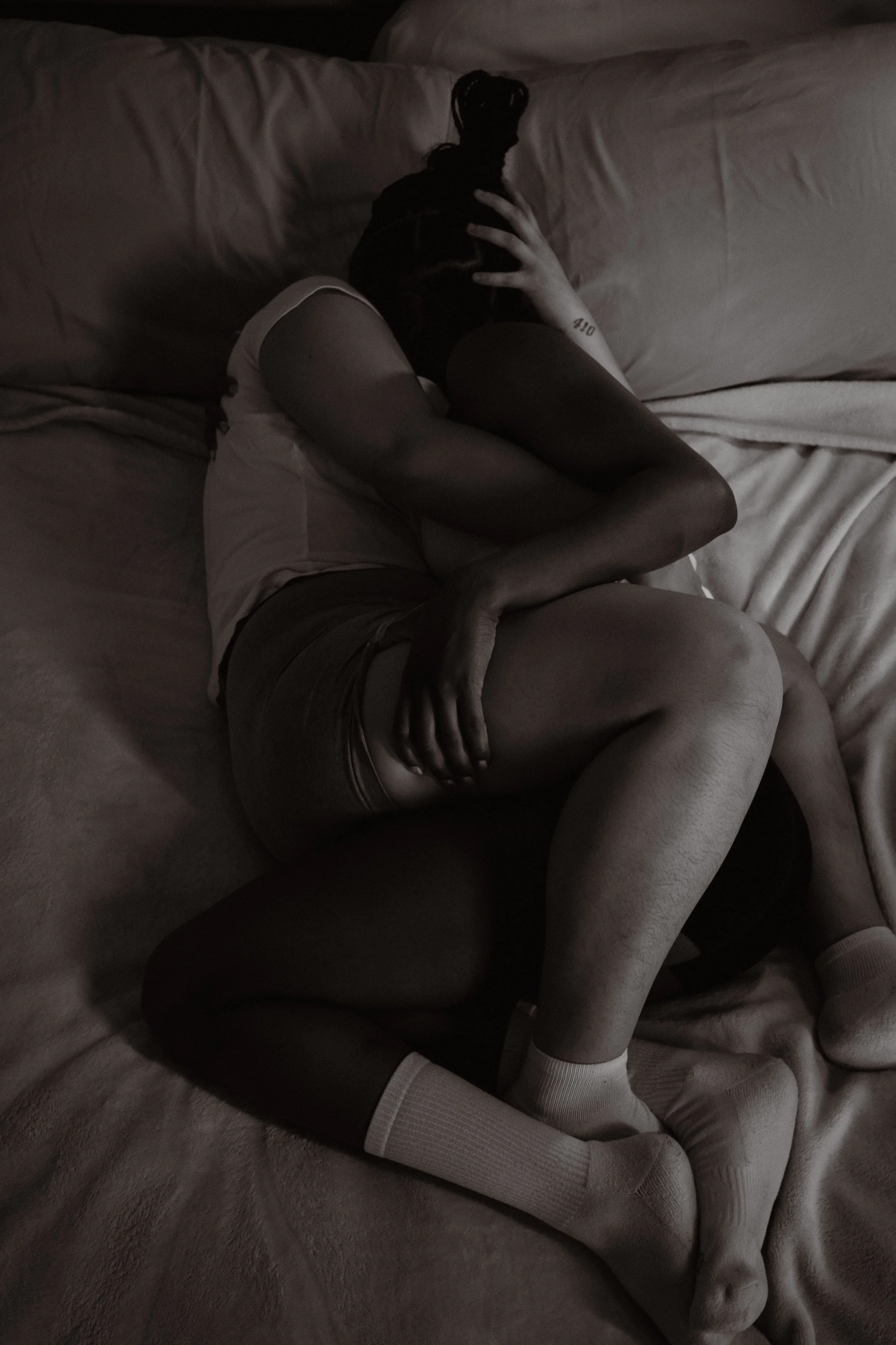 A Black and White photograph where two people are embracing on a bed with two pillows.