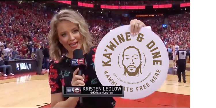 A broadcaster holding a Ka’Wine & Dine sign on the Toronto Raptors court