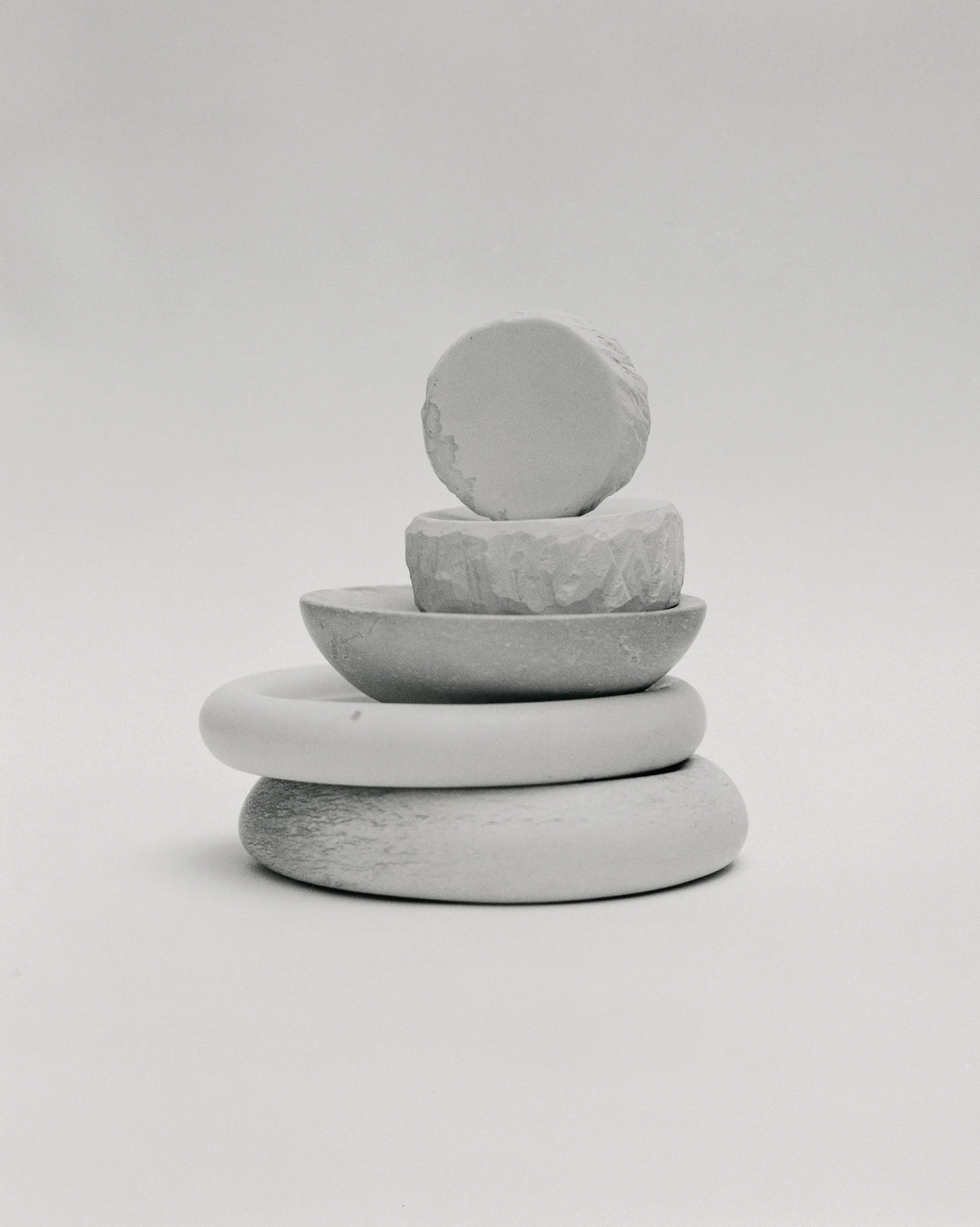 Stack of five smooth, rounded stones in grayscale, arranged vertically on a plain white surface.