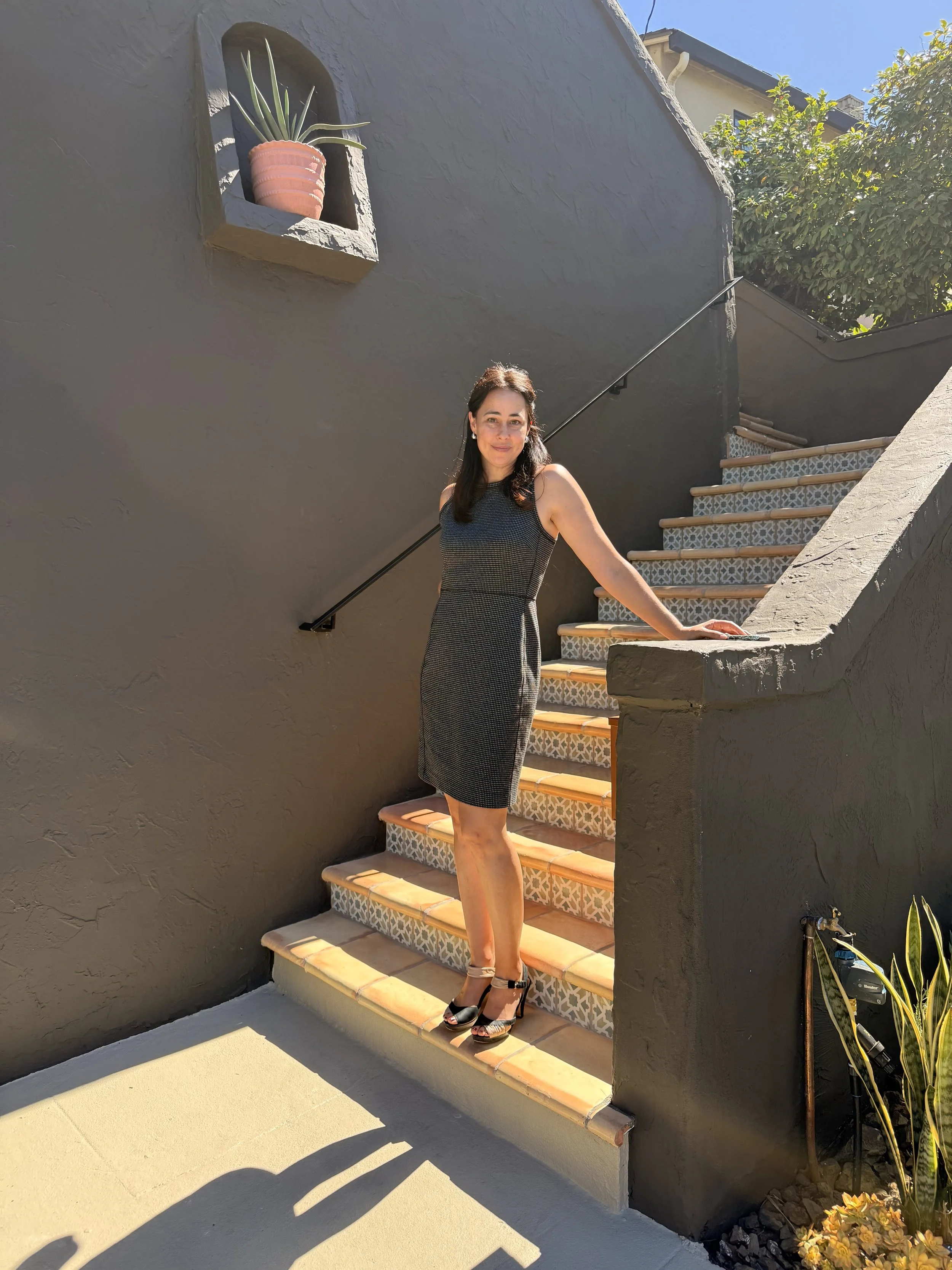 Lindsay Scott, East Bay real estate agent, wearing a grey dress, standing at the entrance of a home on terracotta tile