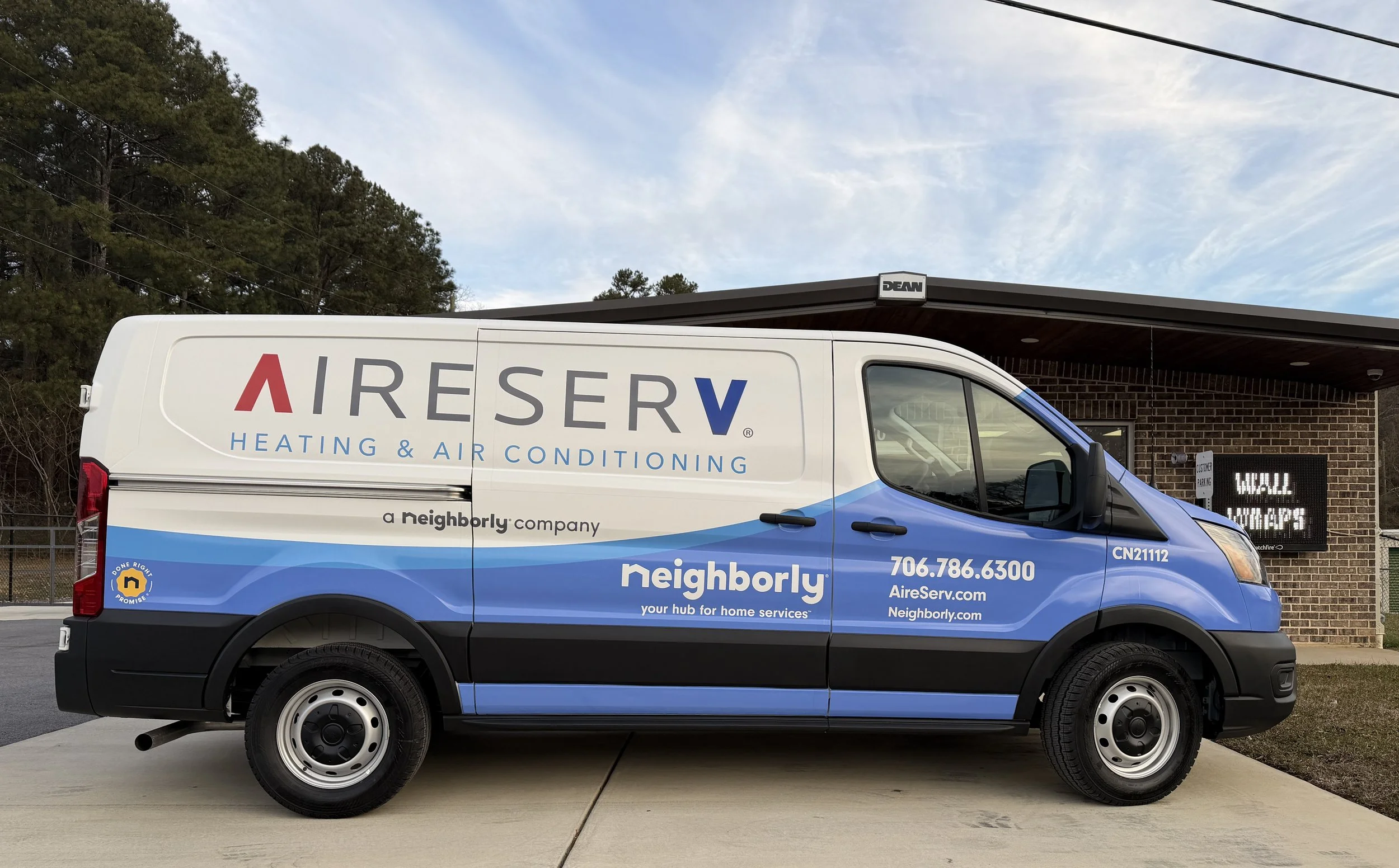 Blue and white company service van parked outside a brick building with an electronic sign in the background.