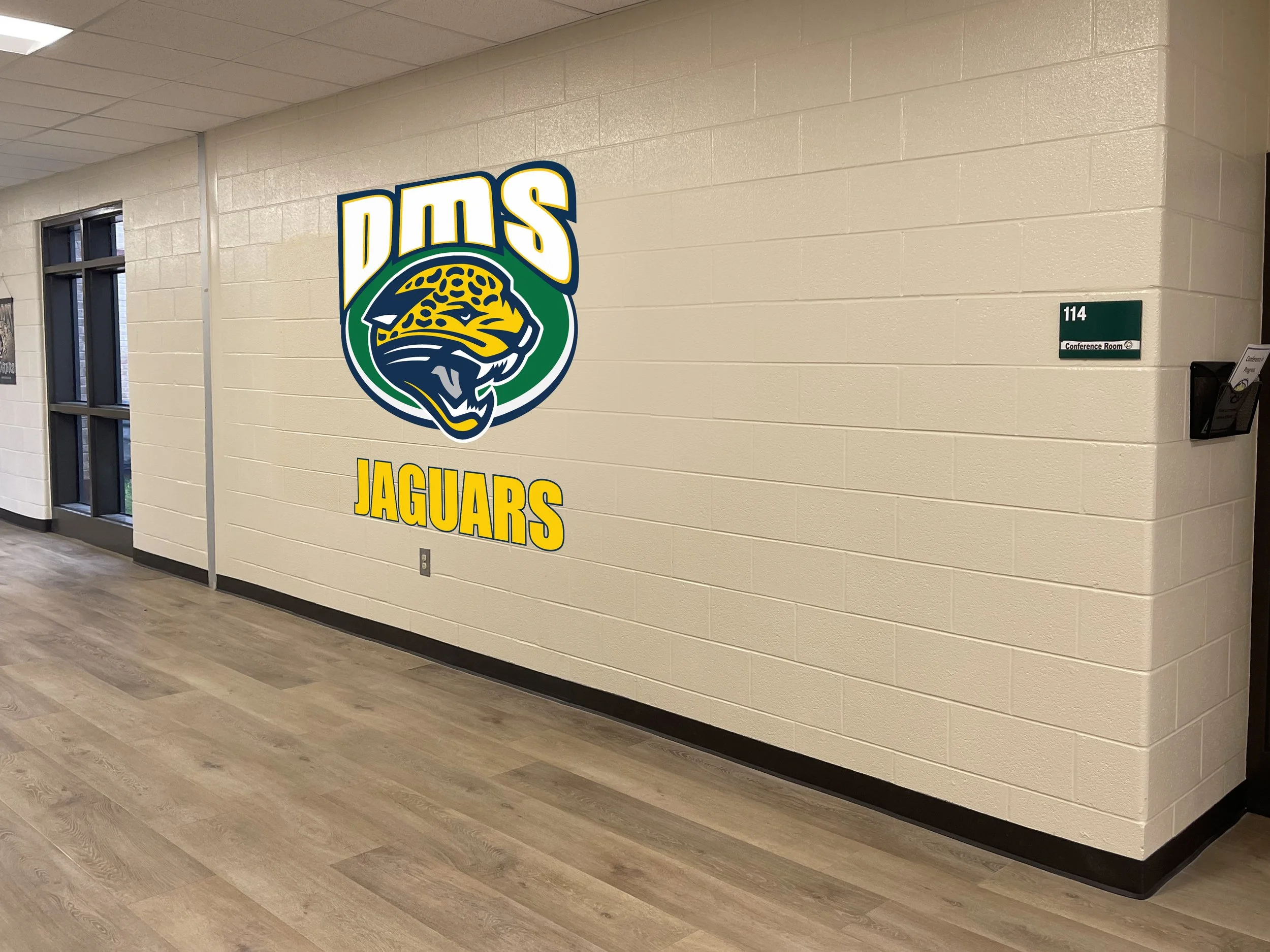 School hallway with a large Jacksonville Jaguars logo on the wall and a room number 114 sign.