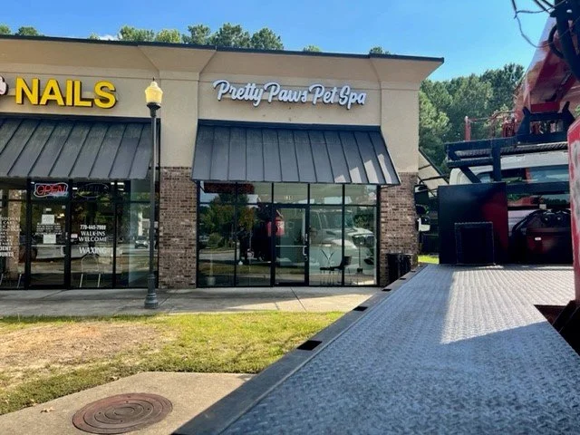Storefront with signs for Nails and Pretty Paws Pet Spa, with glass doors and windows, a brick facade, and a lamppost in front.