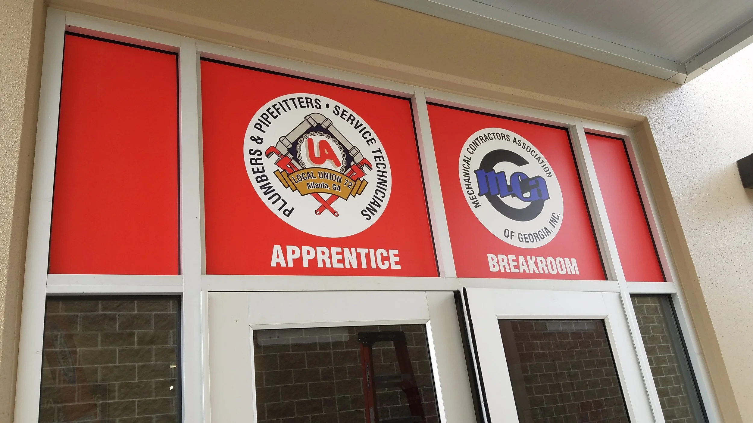 Signs on a door window indicating apprentice and breakroom for a union electrical contractors group.