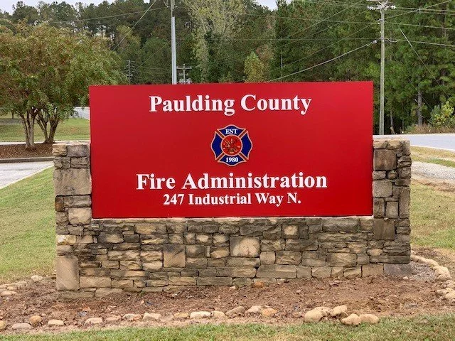 Red sign for Paulding County Fire Administration located at 247 Industrial Way North, with a stone base and surrounded by grass and trees.