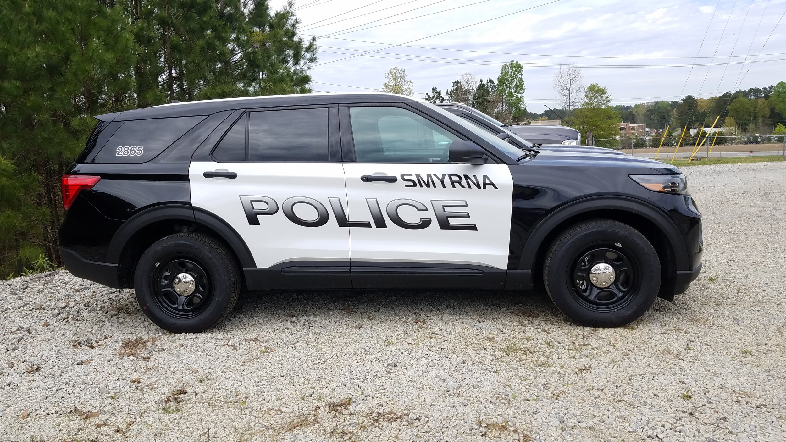 Smyrna Police SUV parked on gravel with green trees and utility lines in the background.